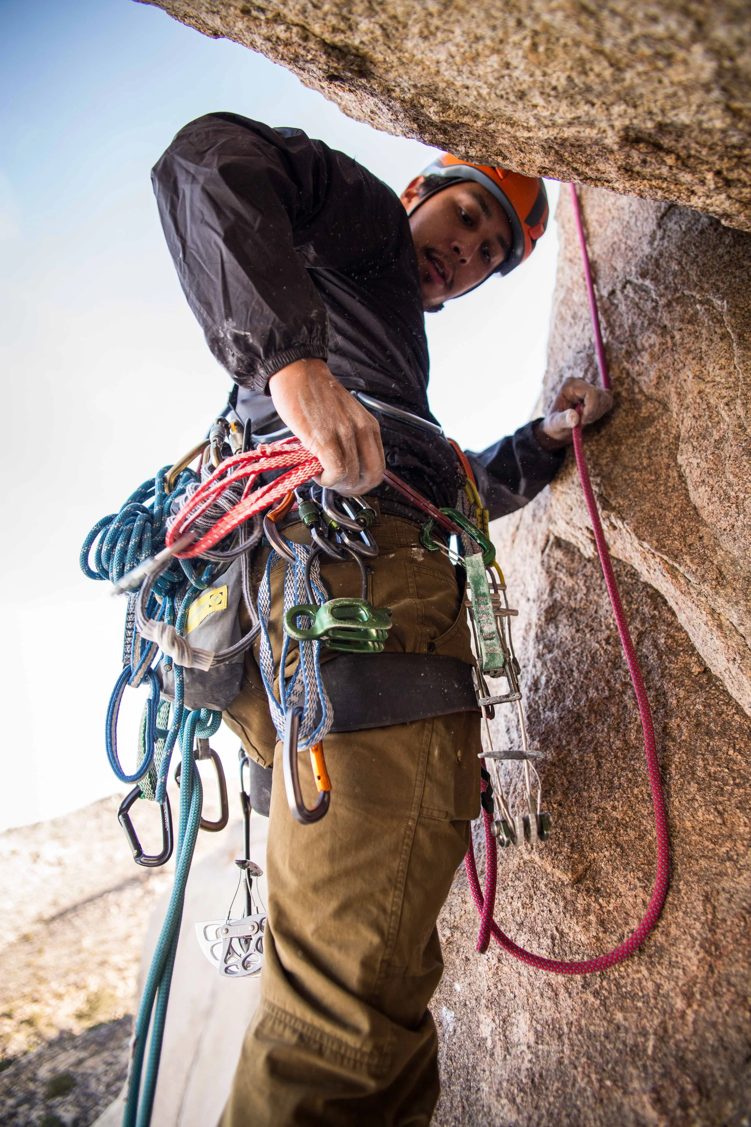 Male rock climber with climbing gear adjusting safety rope on rock face.