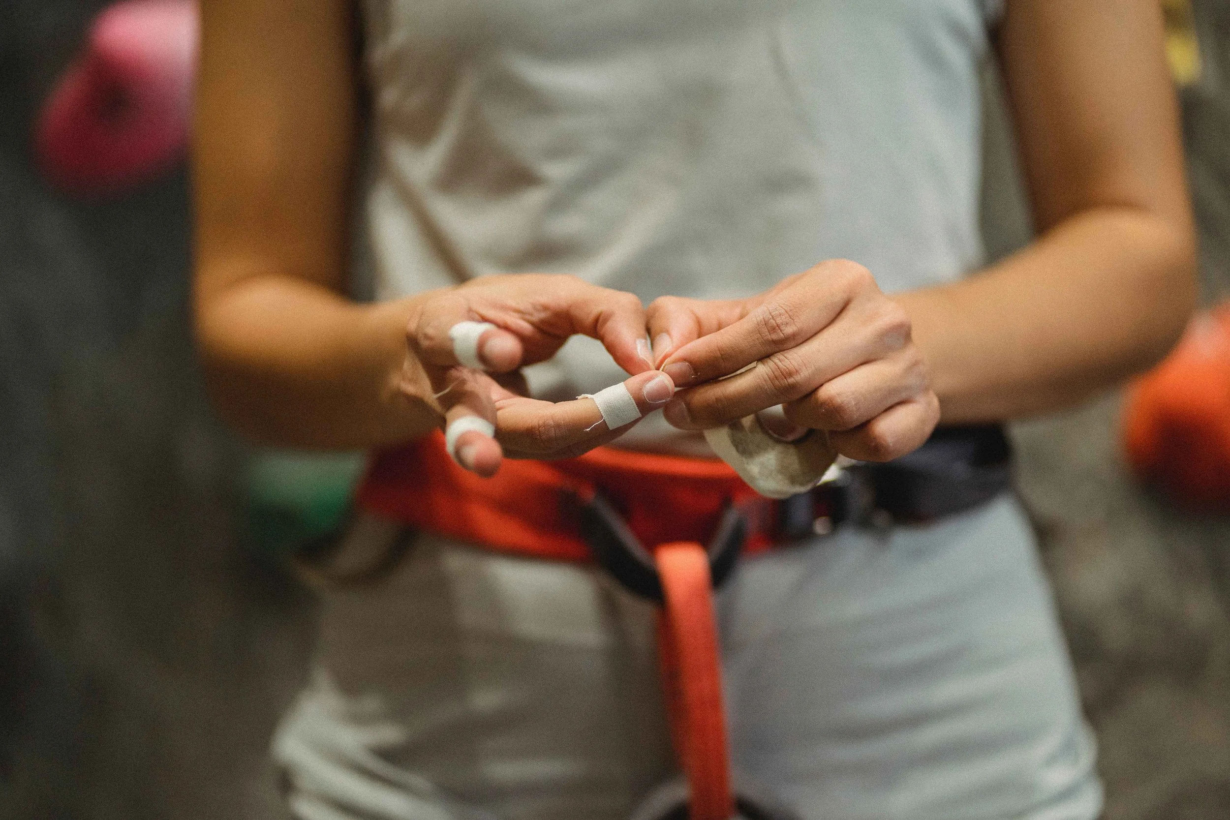 A person with finger tape is putting on climbing or rock climbing gloves.