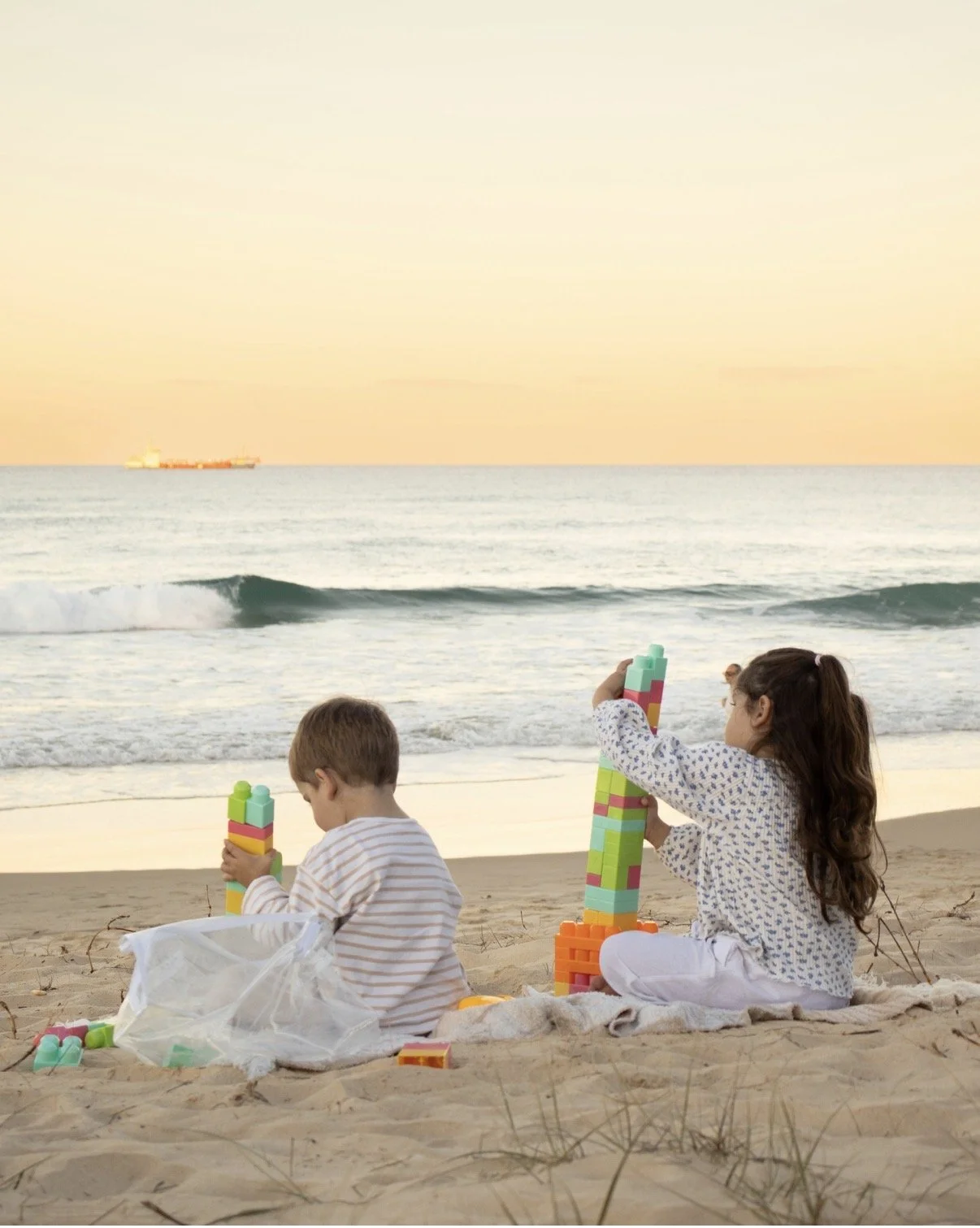 two young children playing with blocks on the beach