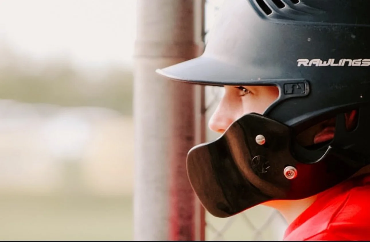 Baseball player wearing a black helmet with a faceguard, looking to the side.