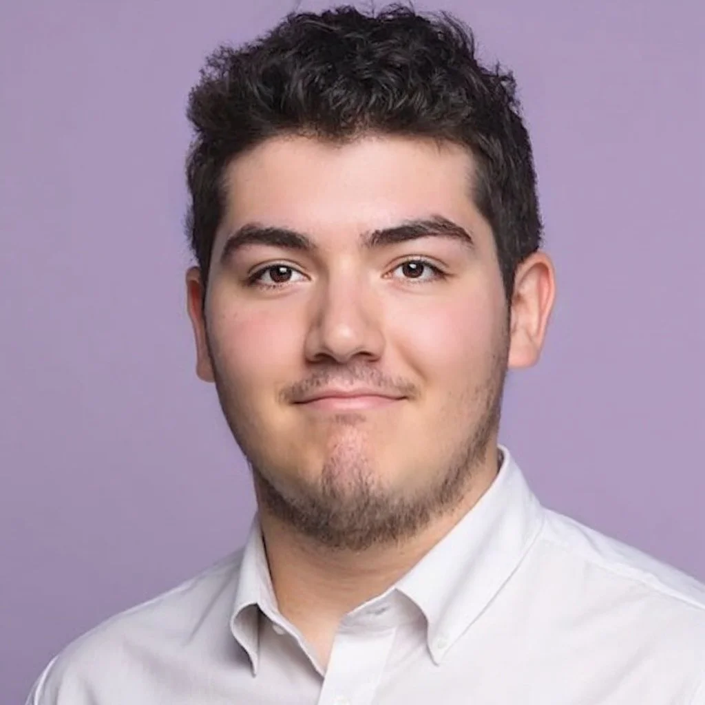 Young man with short hair and light facial hair wearing a white shirt, against a purple background.