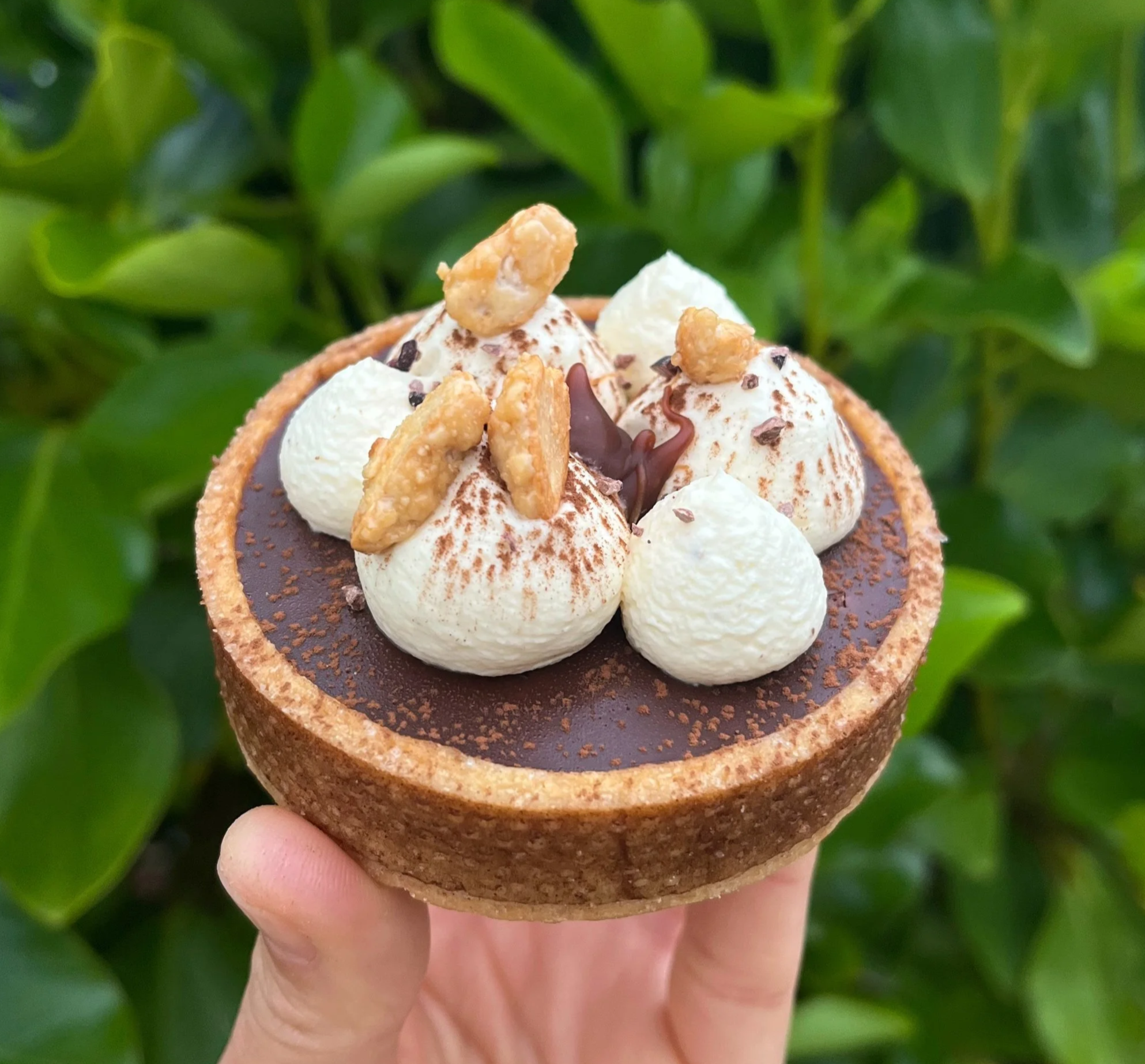 Close-up of a hand holding a chocolate, caramel and peanuts tart, French pastry