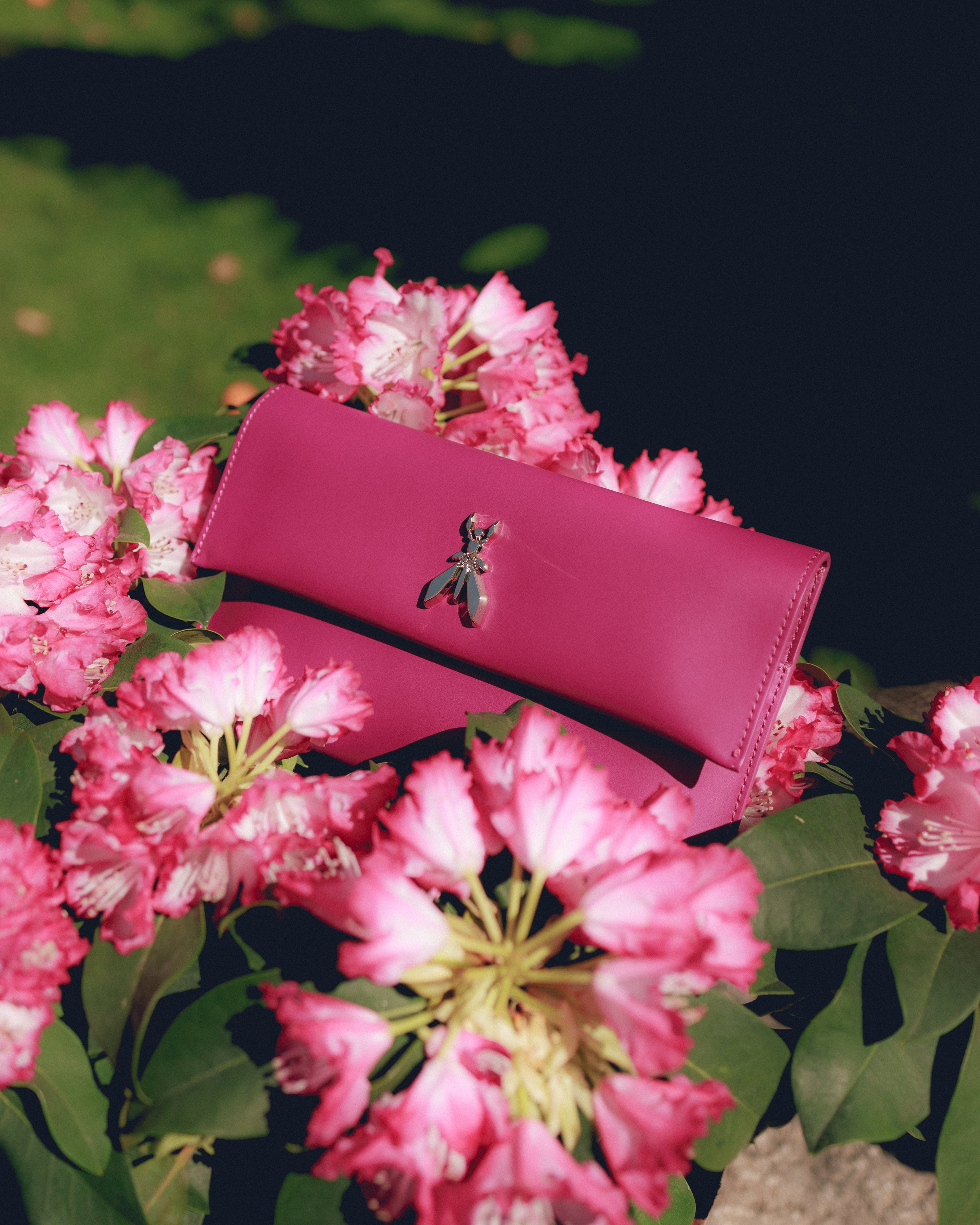 Borsetta fucsia circondata da fiori rosa e foglie verdi.