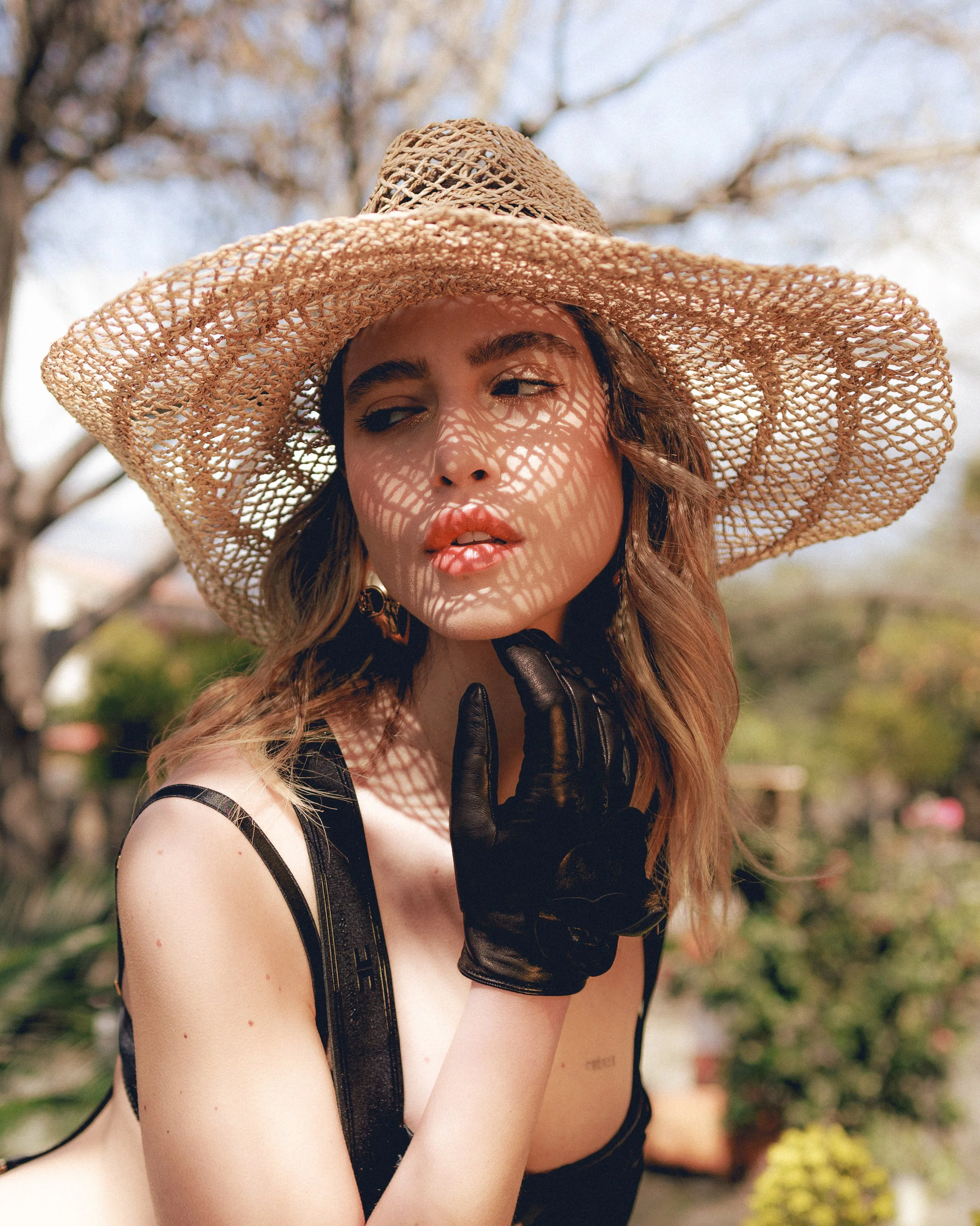 Donna con cappello di paglia e guanti neri in giardino.