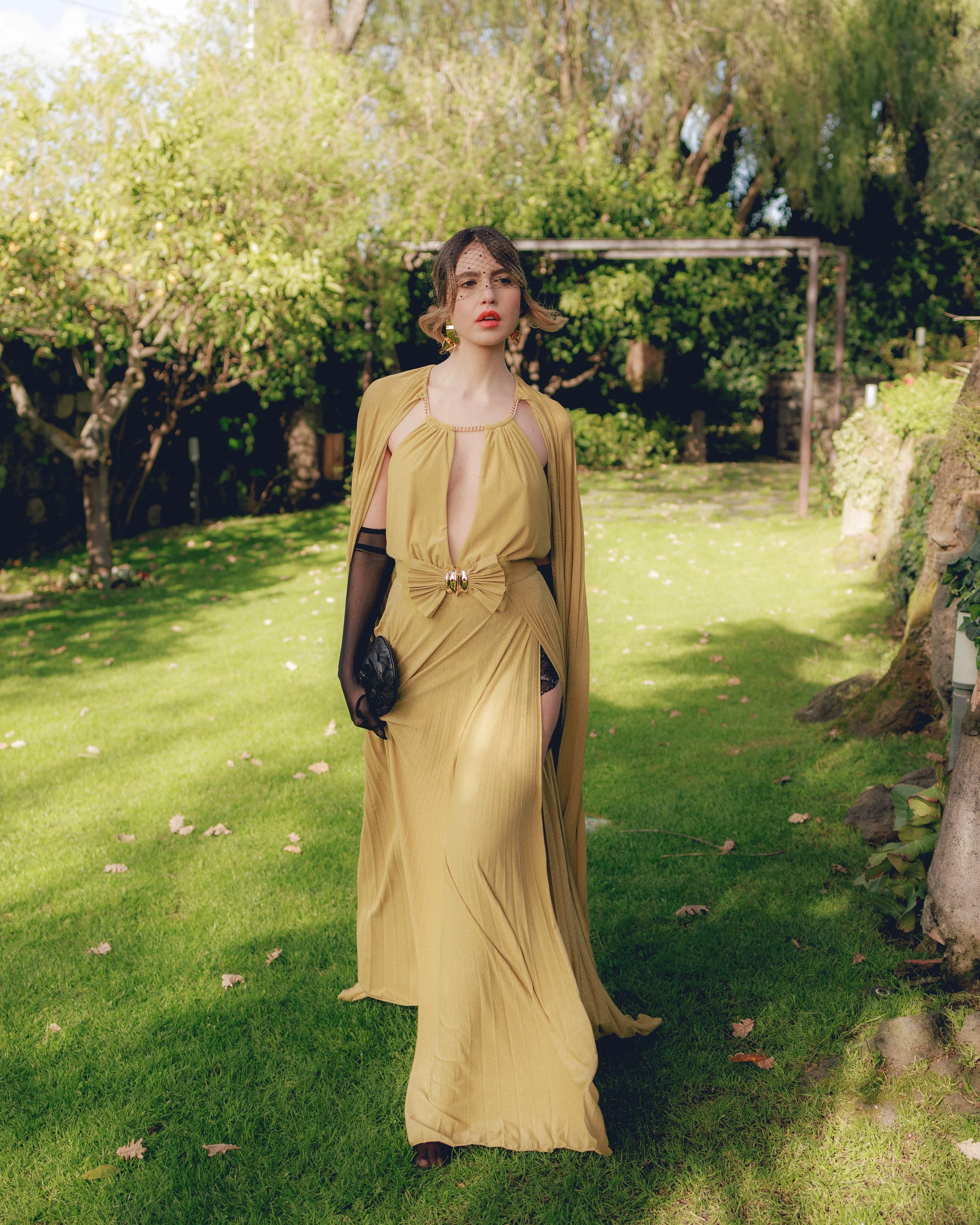 Donna in un abito lungo giallo in un giardino verde con alberi sullo sfondo.