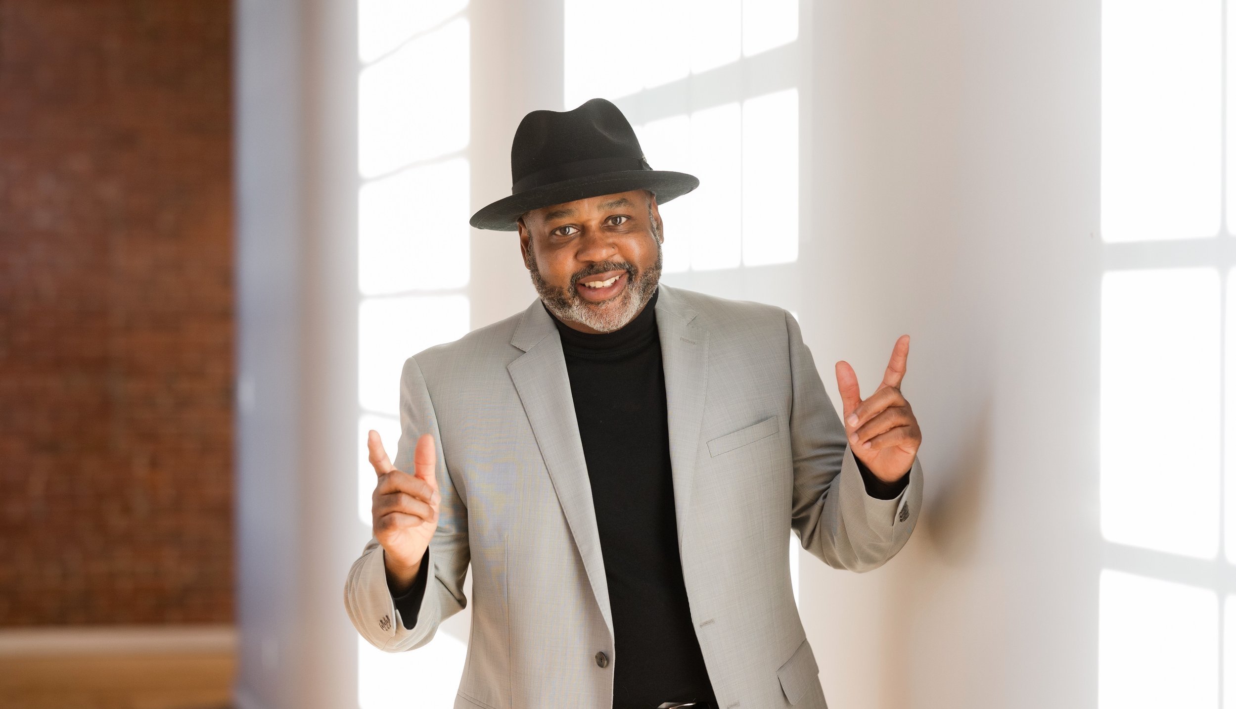 Clayton Craddock smiling in a gray suit and black hat