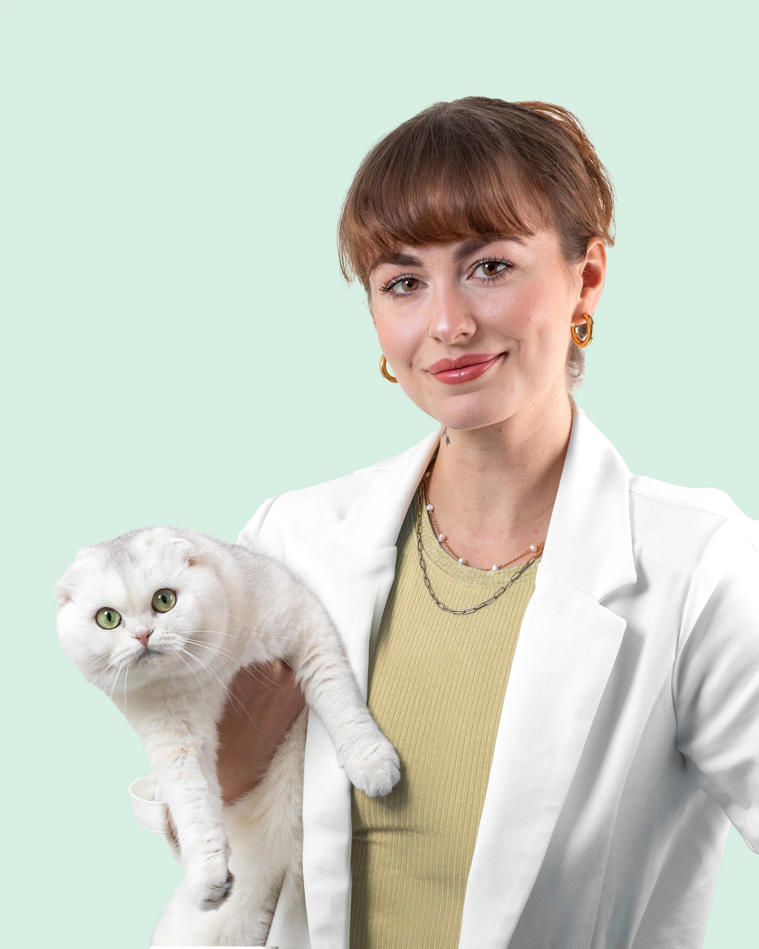 A woman with short brown hair, wearing a white jacket and gold jewelry, holding a white and cream Persian cat with green eyes against a light green background.