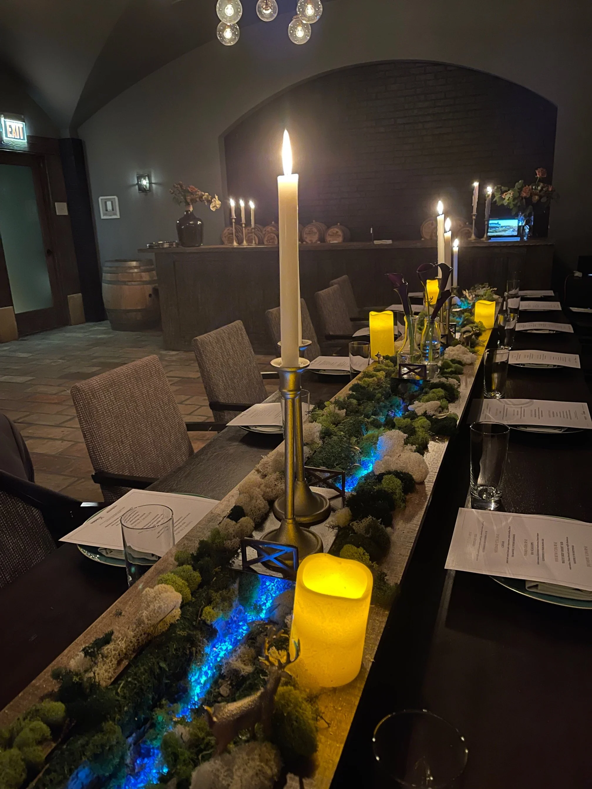 Glenfiddich Table scape Decorated dining table with candles, greenery, and place settings for a formal event in a dimly lit room.