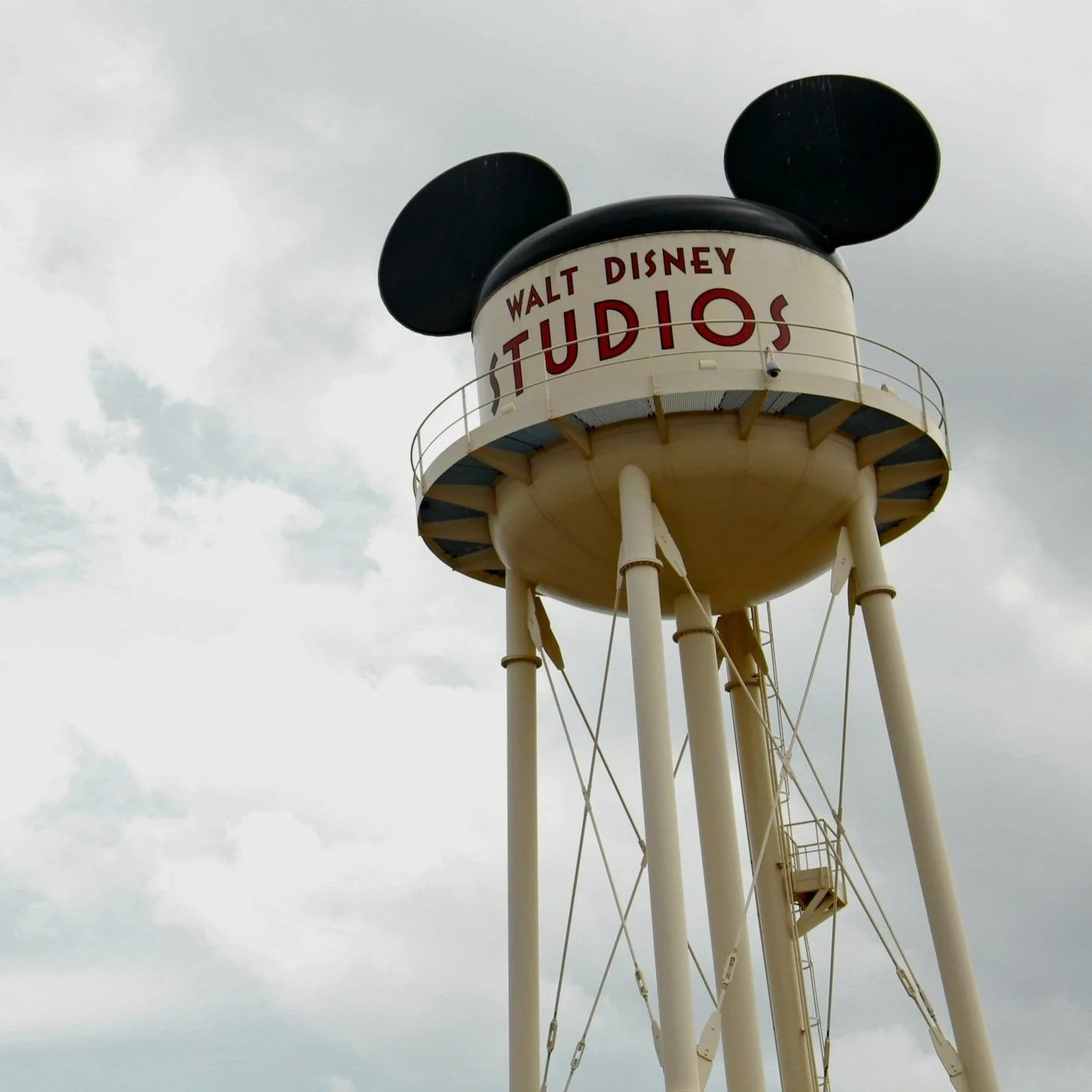 White water tower with "Walt Disney Studios" written on it, featuring Mickey Mouse ears on top, set against a cloudy sky.