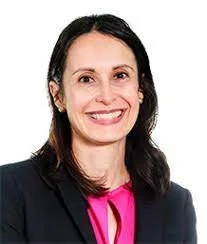 A woman with shoulder-length dark hair, smiling, wearing a black blazer and a pink top, against a white background.