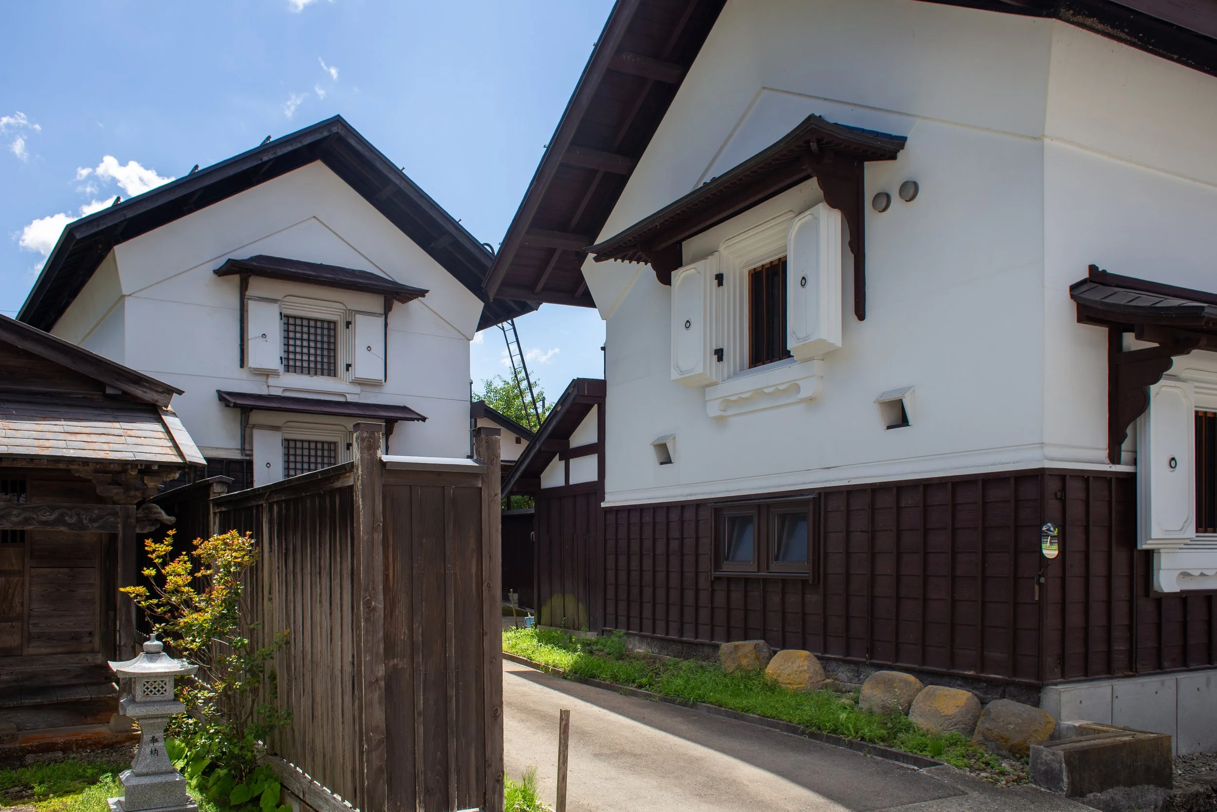 Traditional Japanese houses with white walls, dark wooden accents, and small, barred windows, under a clear blue sky.