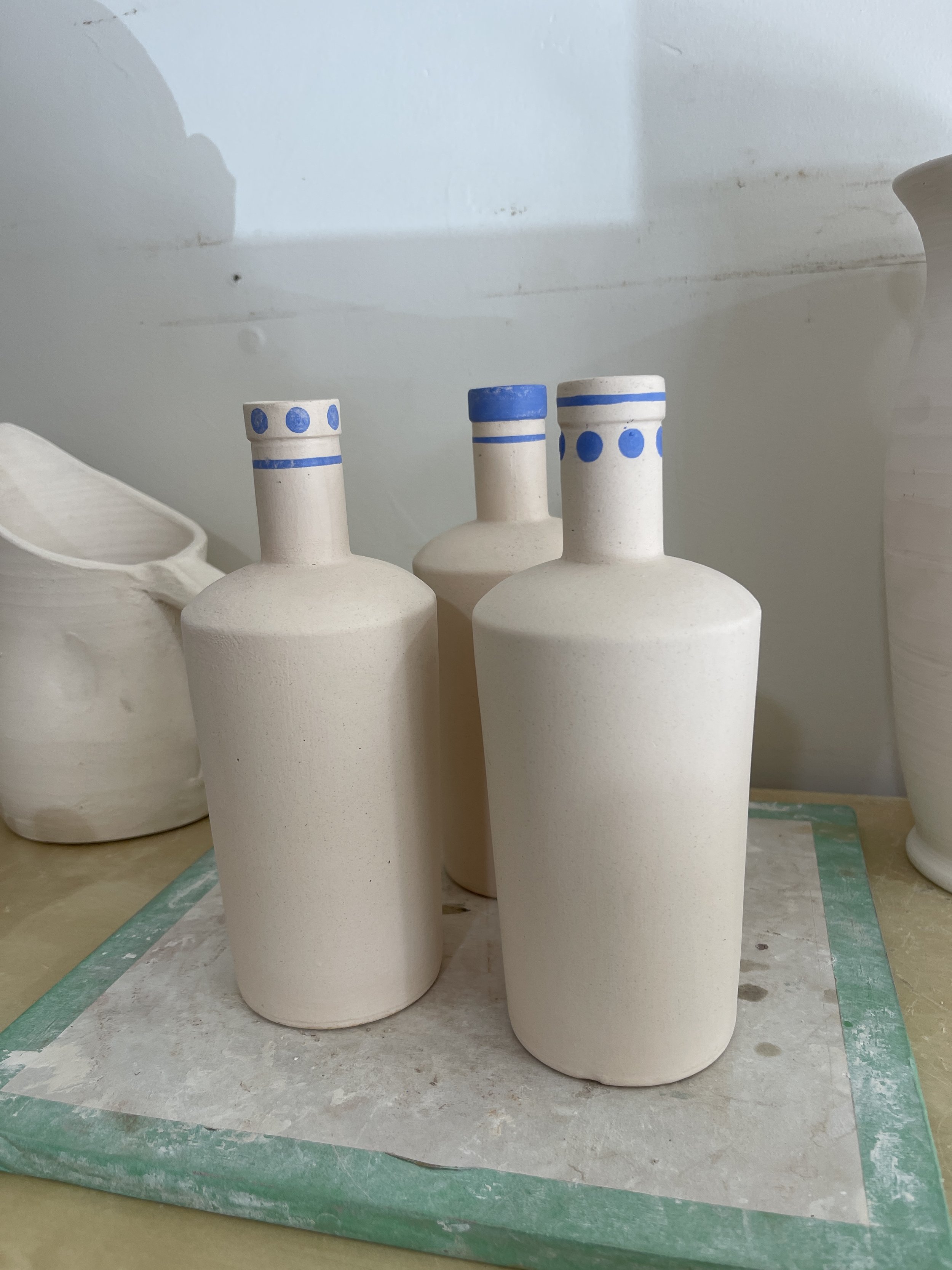 Three ceramic bottles with blue decorative bands on their necks, placed on a surface next to other pottery items.