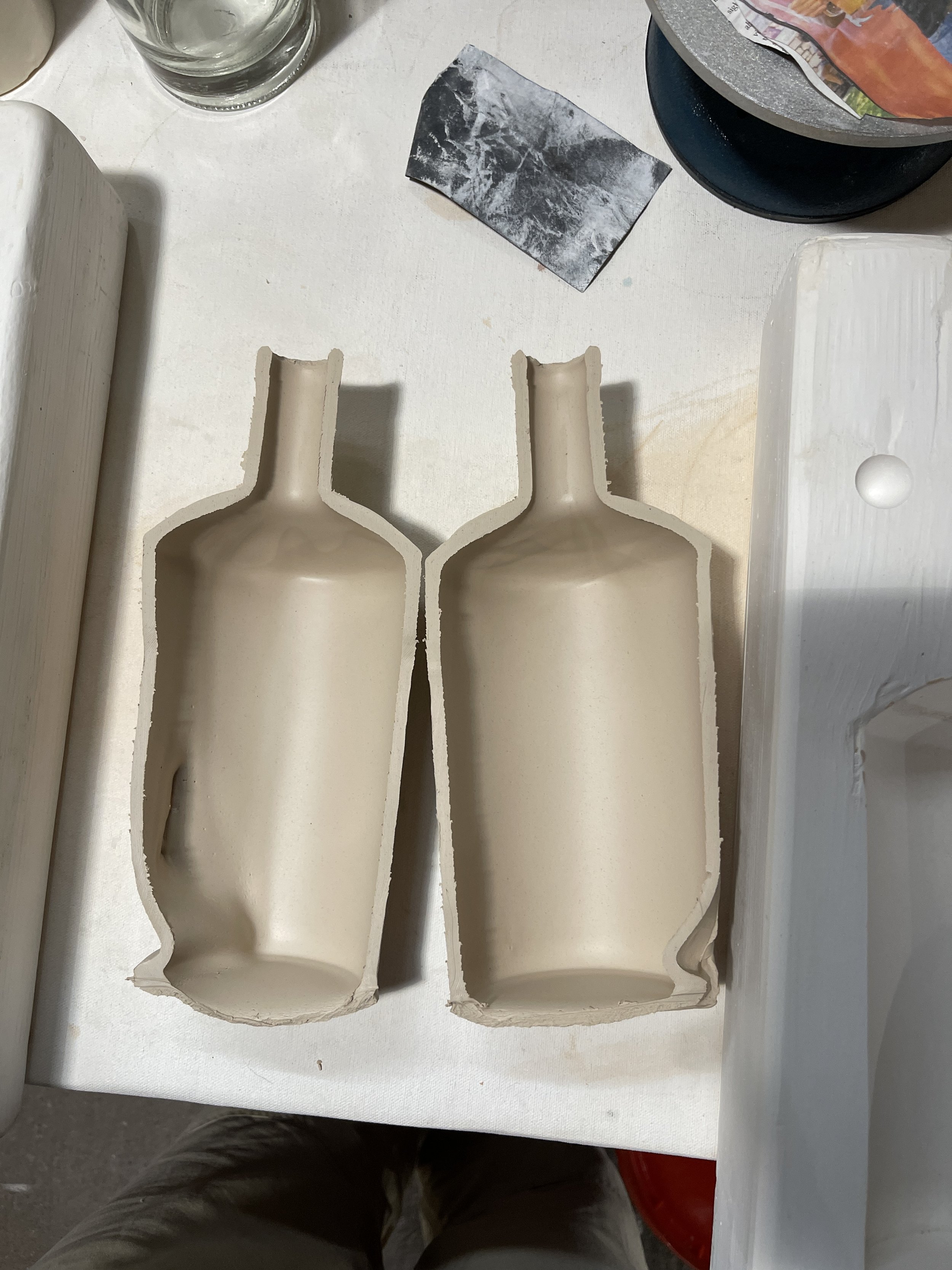 Two halves of a ceramic bottle mold on a table with various crafting tools and materials.