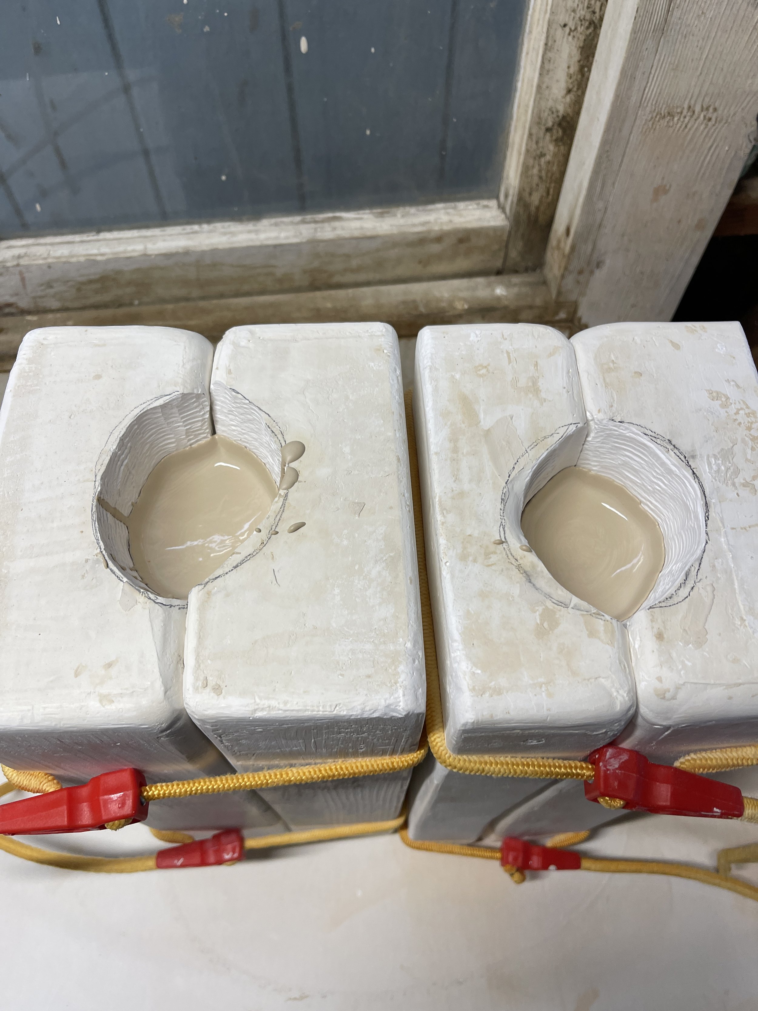 Two rectangular plaster molds secured with straps, containing a beige liquid material, possibly for ceramic casting.