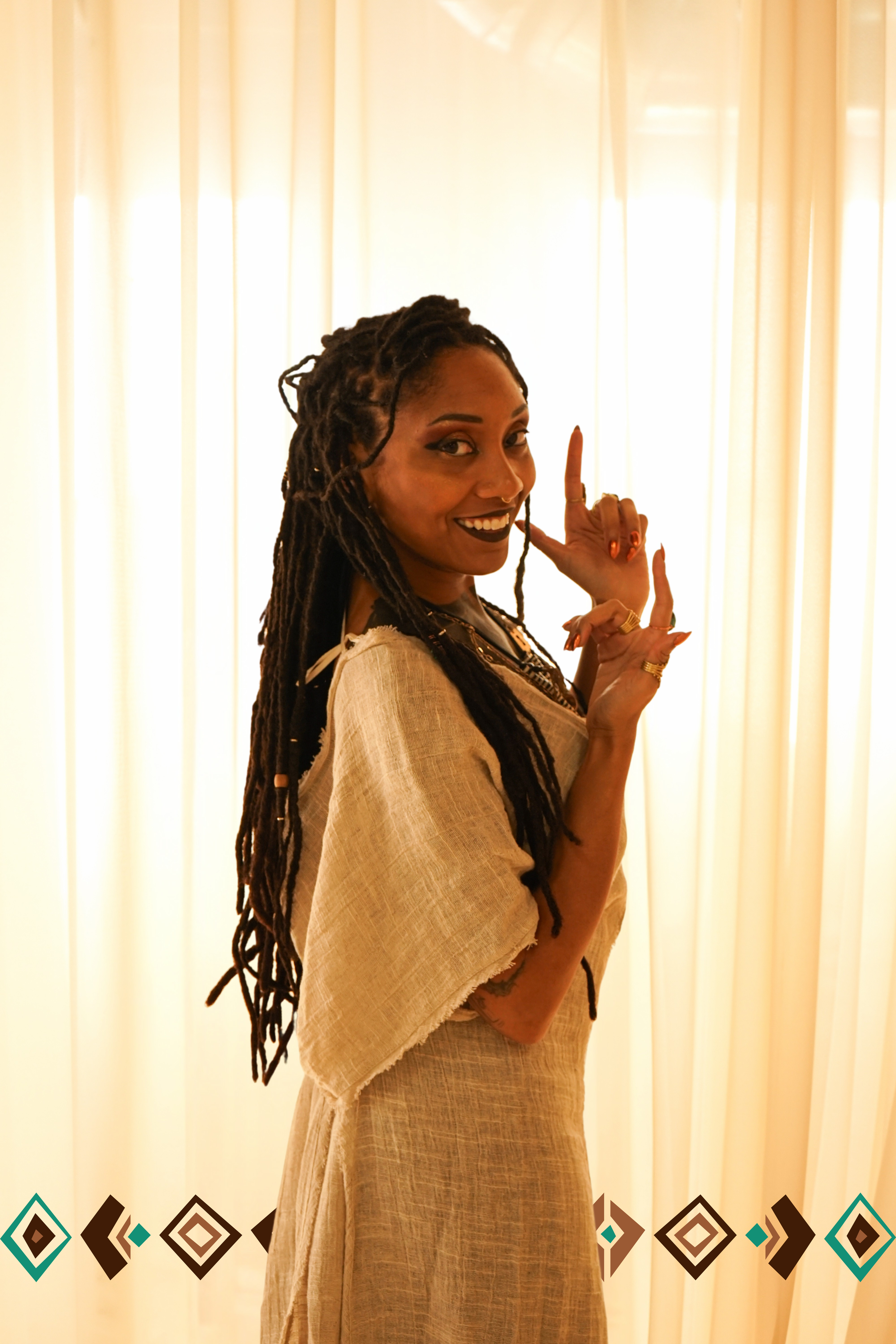 Asha Mahari with braided hair and sacred adornments, standing in stillness with rings and beige ceremonial dress — embodying divine presence and soul remembrance.