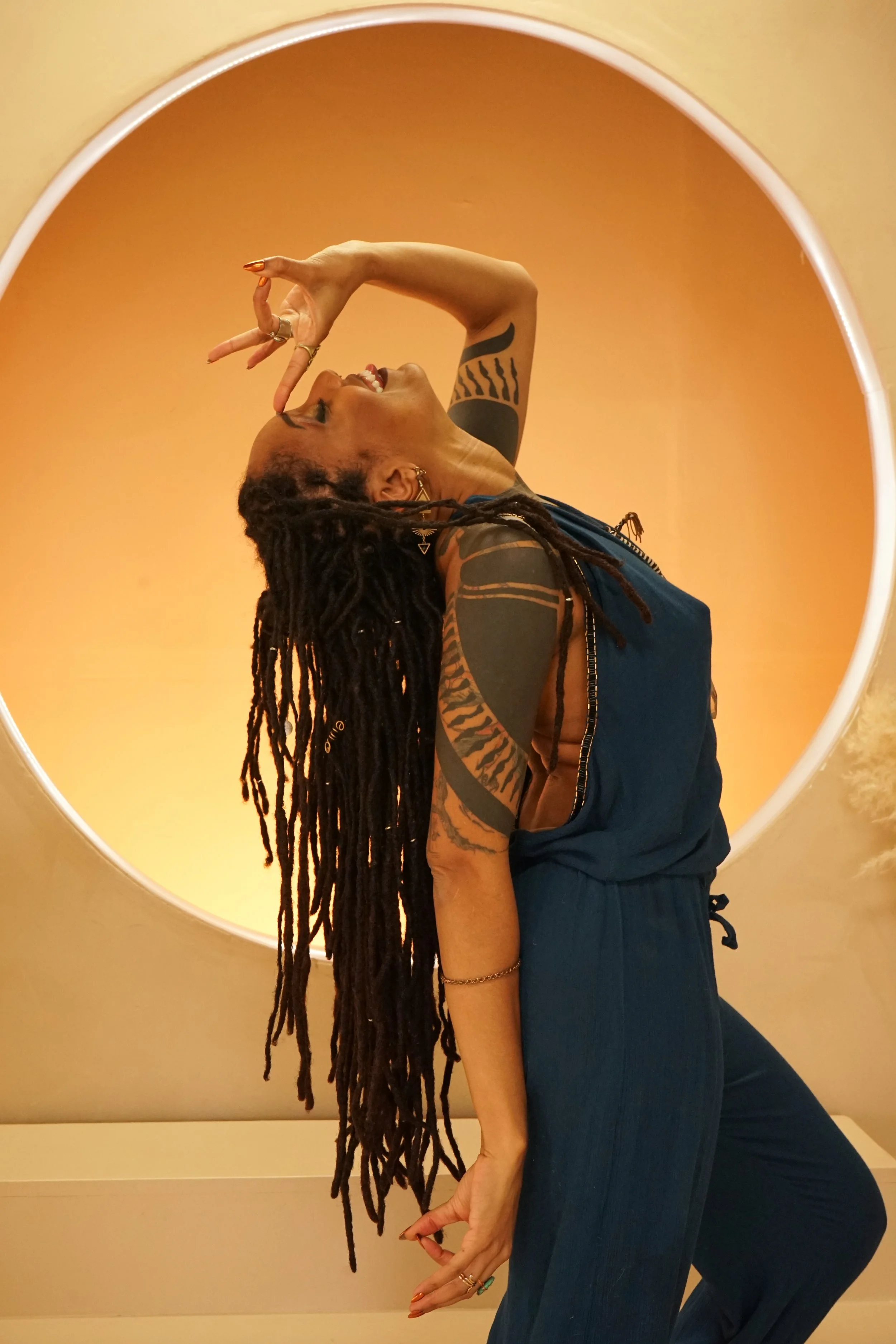 Asha Mahari dancing in flow, adorned in beige ceremonial wear, surrounded by soft light and sacred symbols — invoking liberation and embodiment.