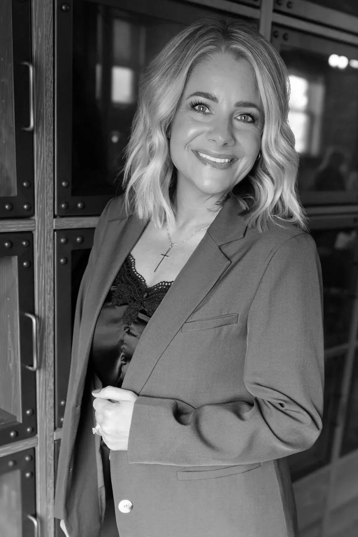 Smiling woman in a blazer and lace-trimmed top standing indoors