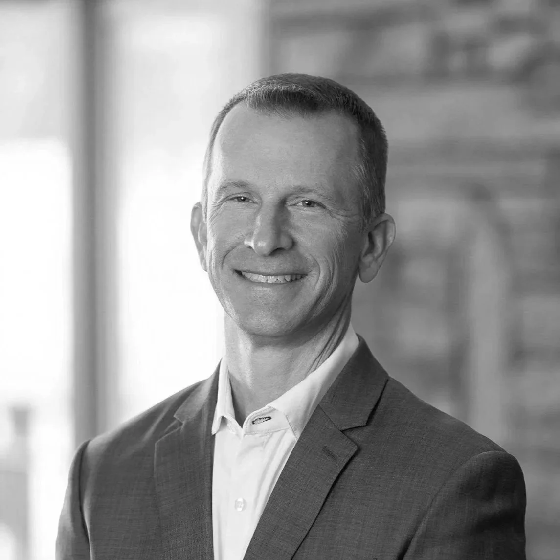 Black and white portrait of a smiling man in a suit, indoors with a blurred background.