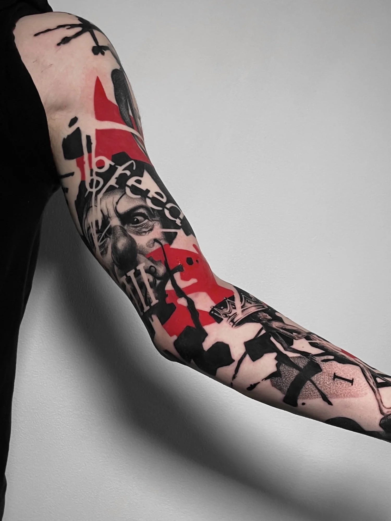 Tattoo sleeve featuring a portrait of a man with glasses and face markings, with bold black, red, and flesh-colored elements.