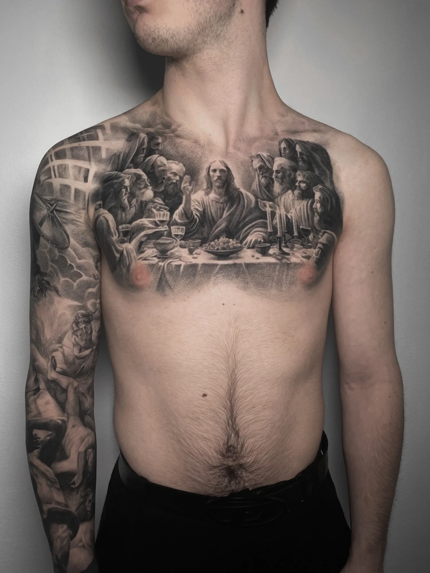 Tattoo of Jesus Christ at the Last Supper on a man's chest, with other religious images on the man's arm.