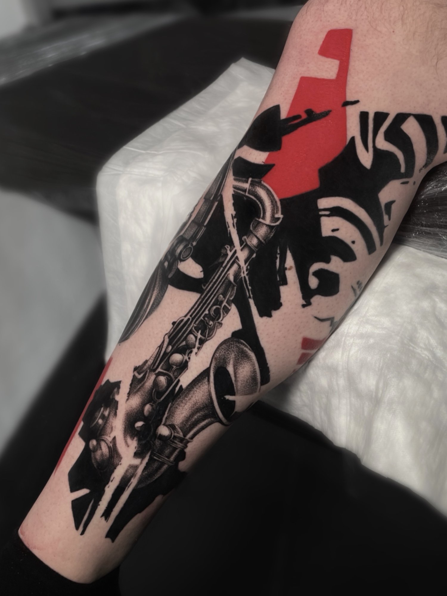 Tattoo of a saxophone on a person's arm with stylized red and black design elements.