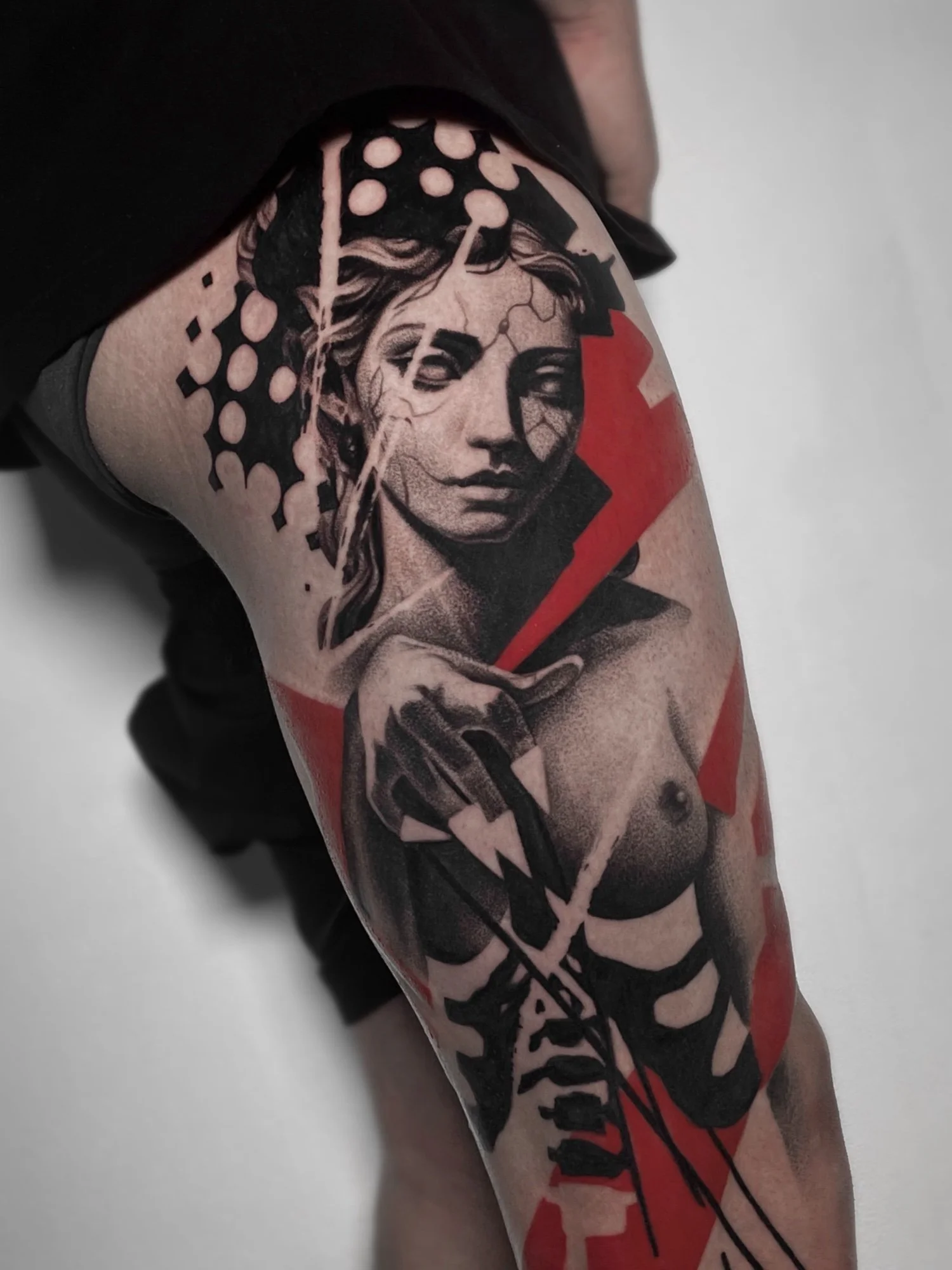 Tattoo of a woman's face with geometric and abstract design elements, including black shapes and red accents.