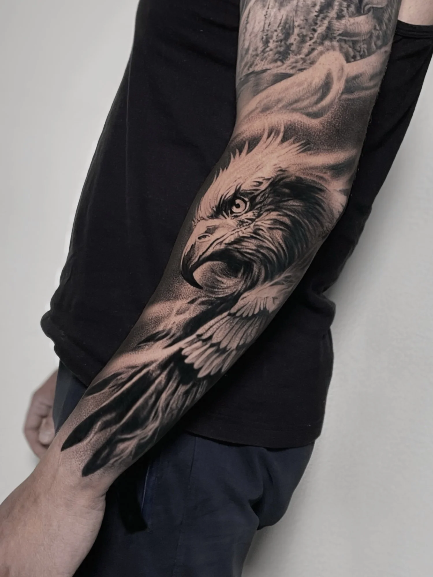A close-up of a person's arm with a detailed black and gray tattoo of a wolf's face, extending from the shoulder to the wrist, wearing a black shirt.