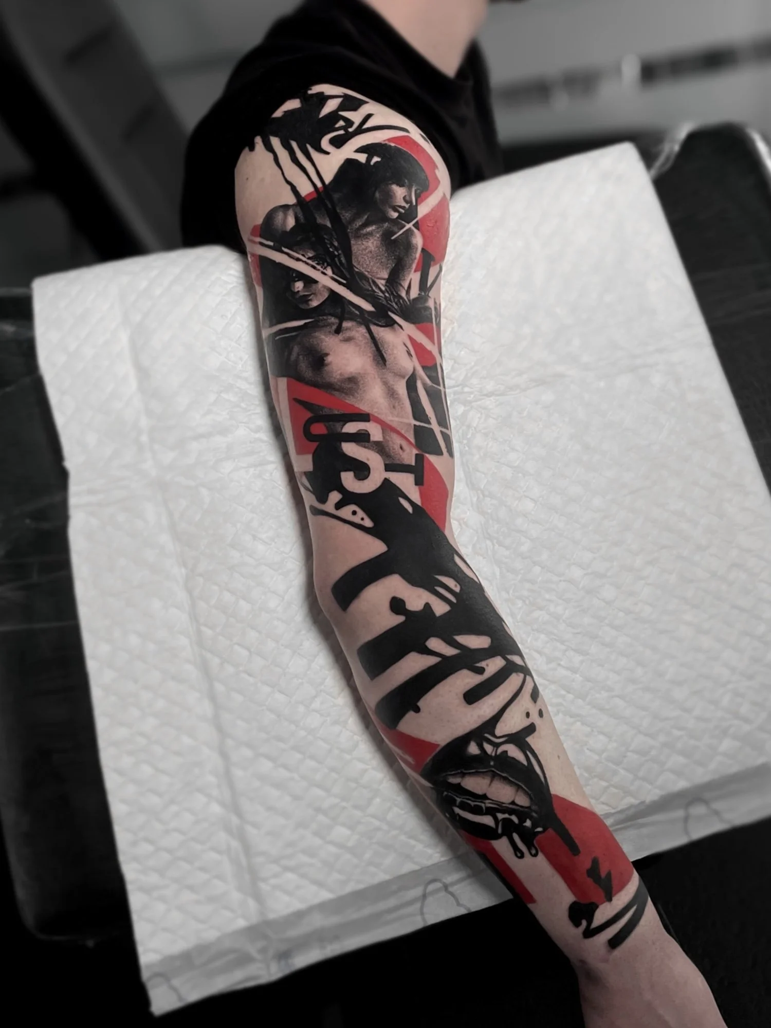 A person's arm with a colorful tattoo depicting a woman with dark hair, holding a dagger in her mouth, with bold black and red design elements.