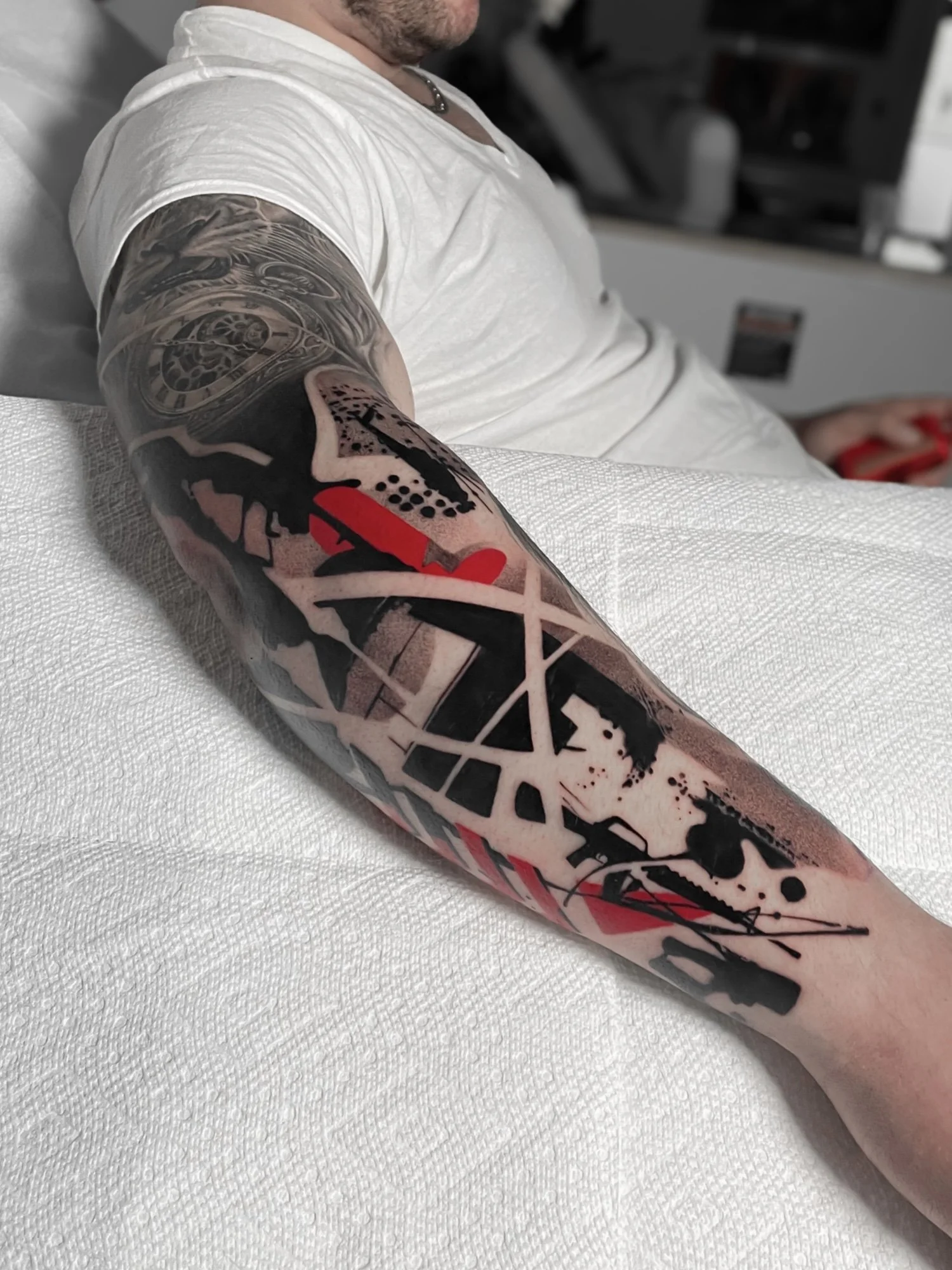 A person's arm with elaborate black, red, and white tattoo art featuring clock gears, abstract patterns, and shading.