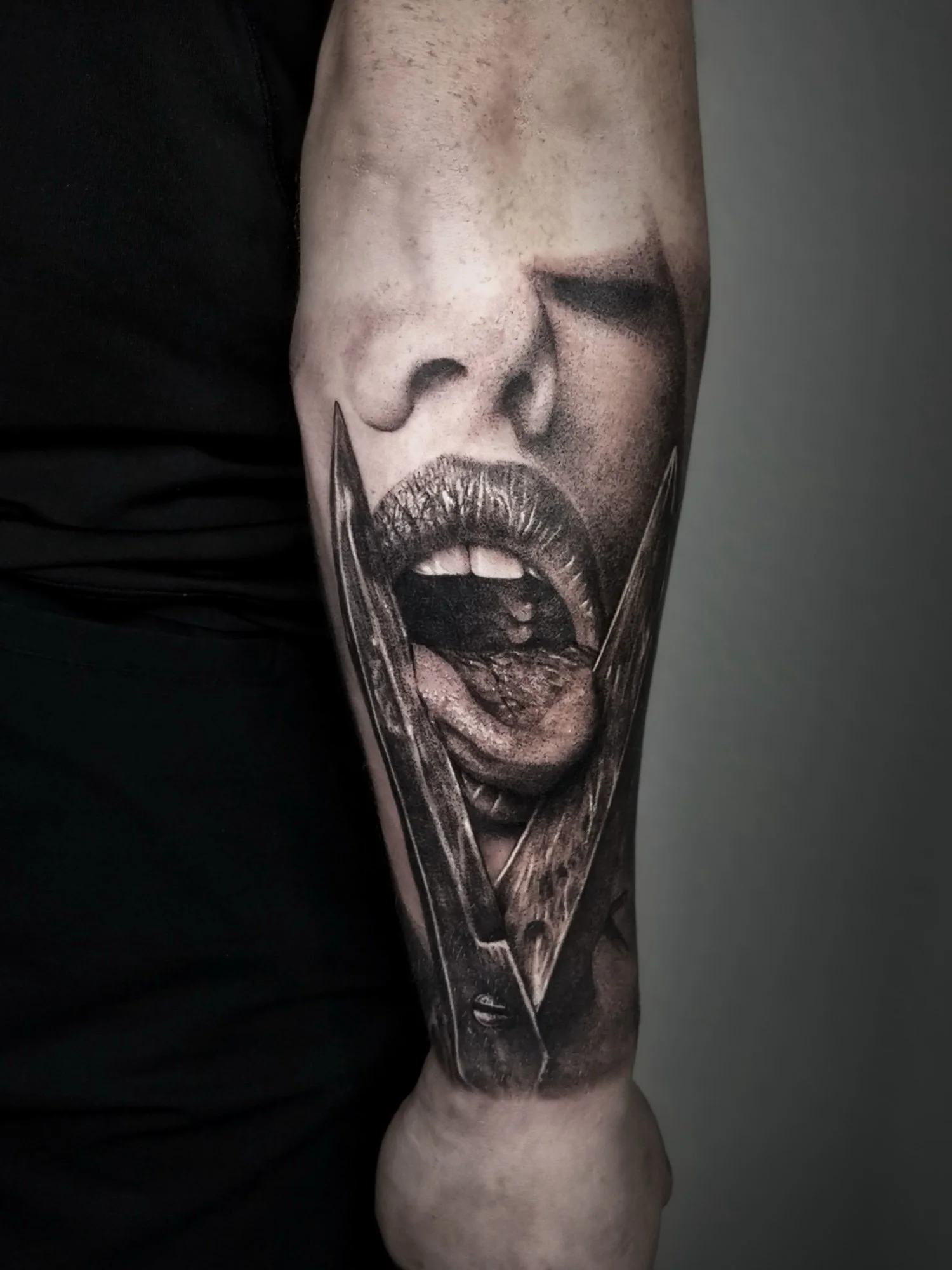 Close-up of a person's arm with a detailed black and gray tattoo of a woman's face with her mouth open, seeming to scream or yell.