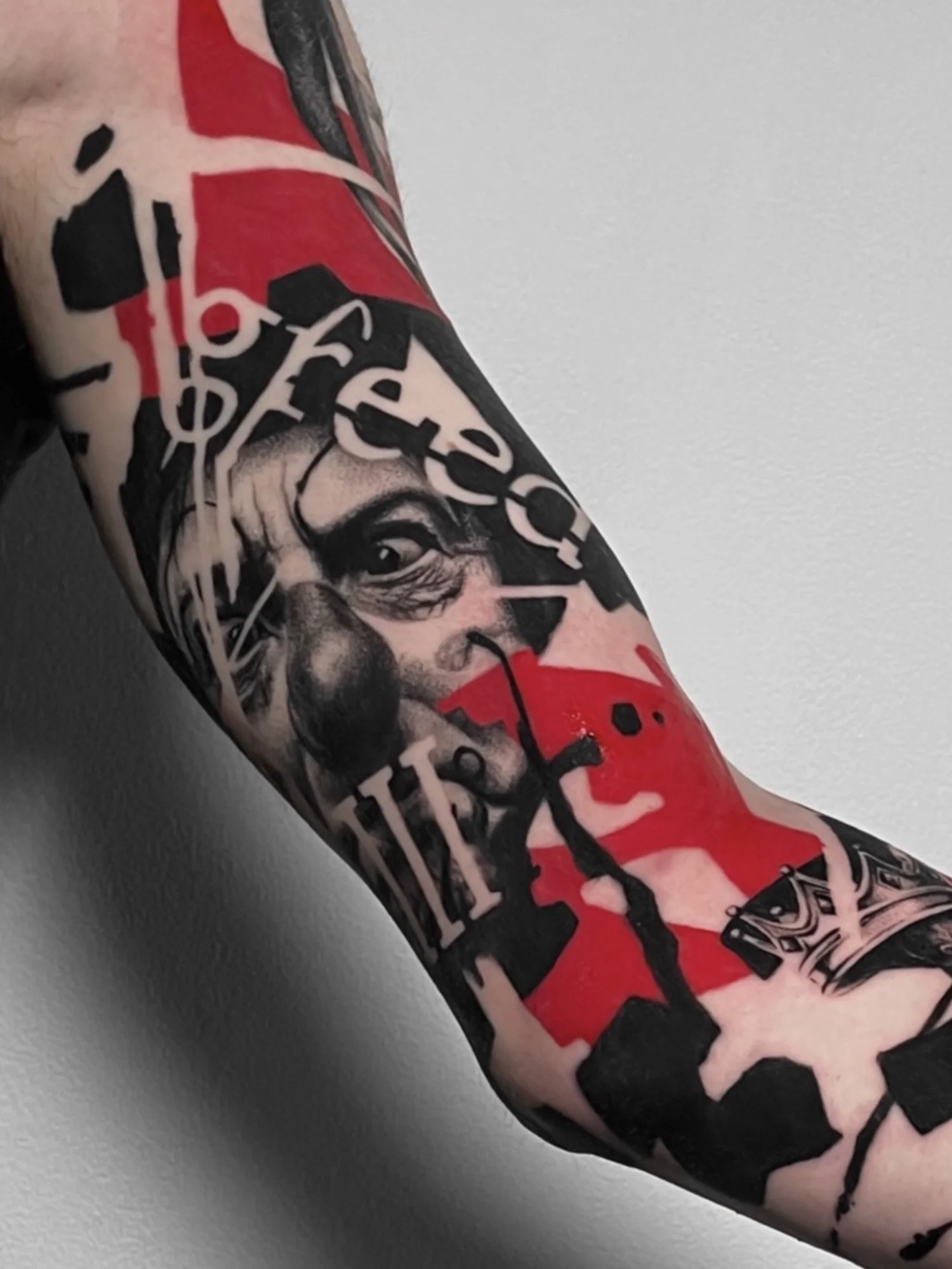 Close-up of a colorful tattoo on a person's arm, featuring a woman's face, abstract shapes, and text design elements.