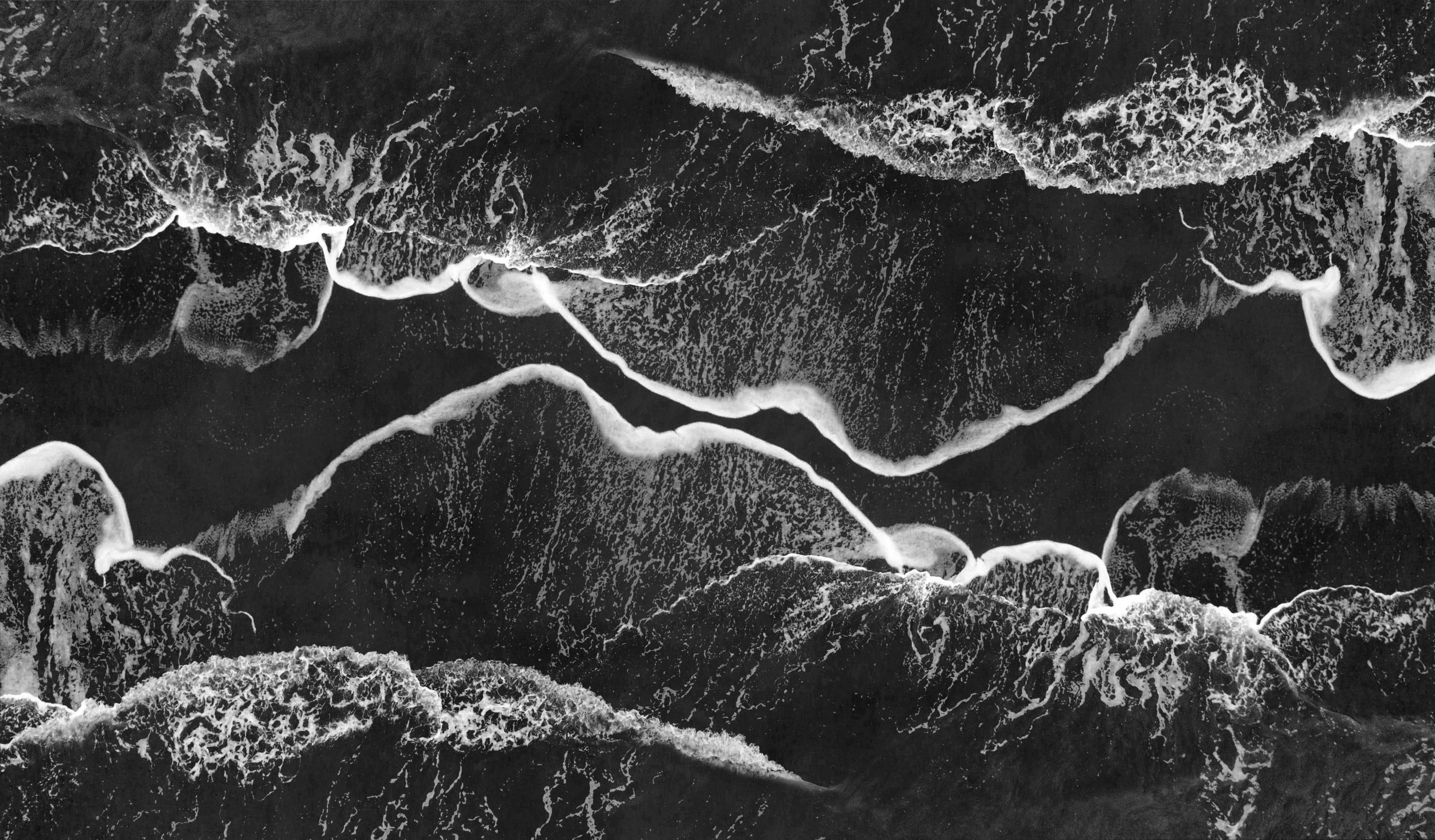 Black and white aerial photo of ocean waves crashing on the shore.