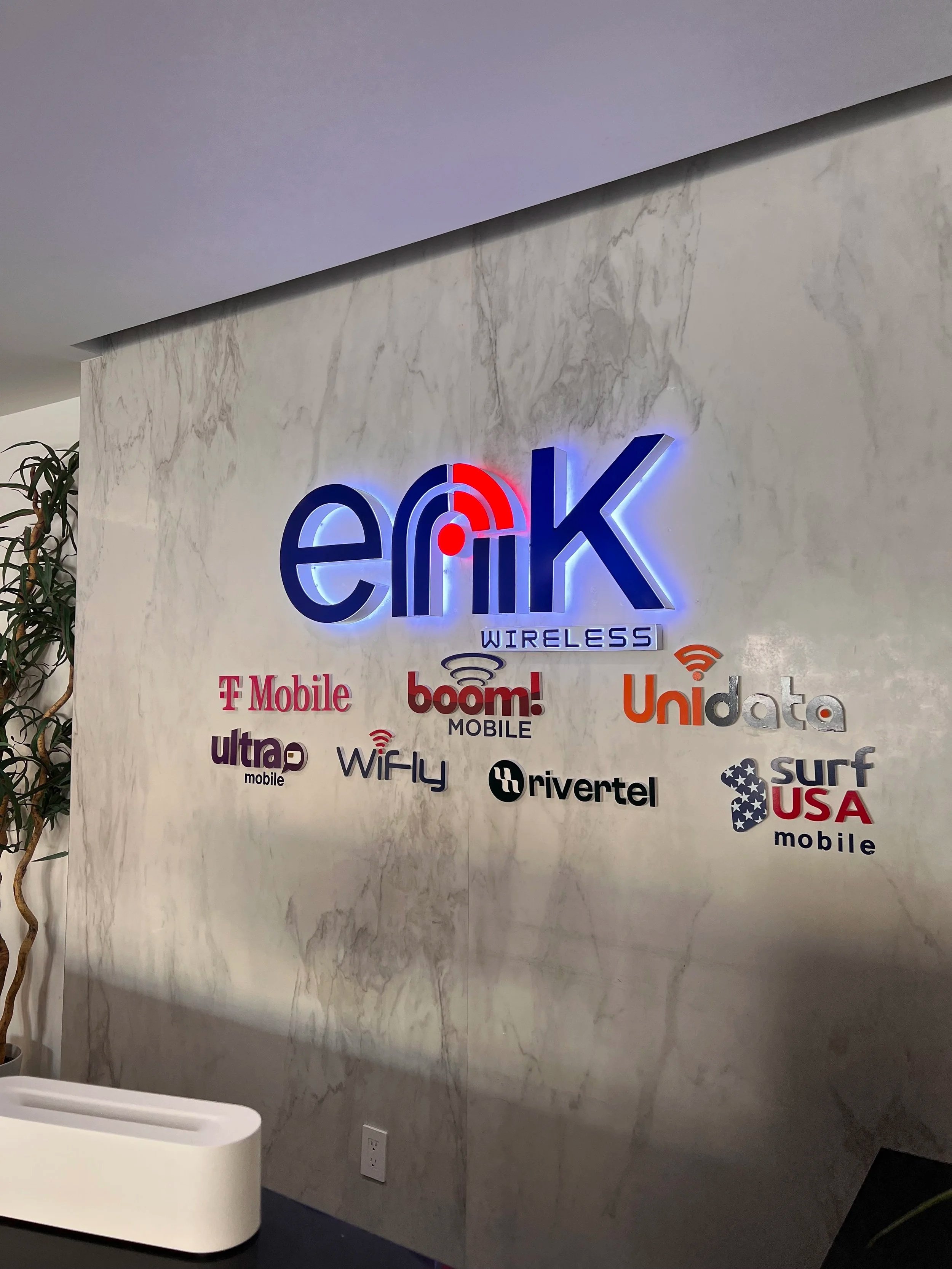 Sign with the logo of Enik Wireless and logos of various mobile service providers including T-Mobile, Boom Mobile, Ultra Mobile, WiFly, Rivertel, Unidata, Surf USA Mobile, with some logos illuminated with LED lighting.