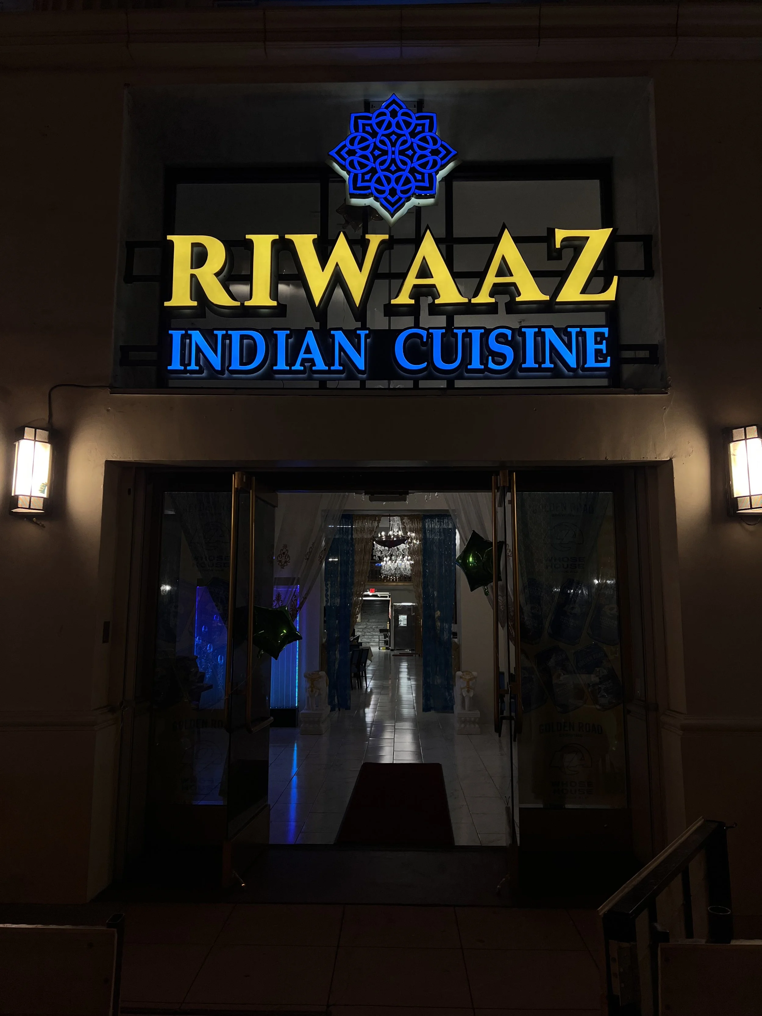 Nighttime view of the entrance to Riwaz Indian Cuisine restaurant with illuminated signboard.