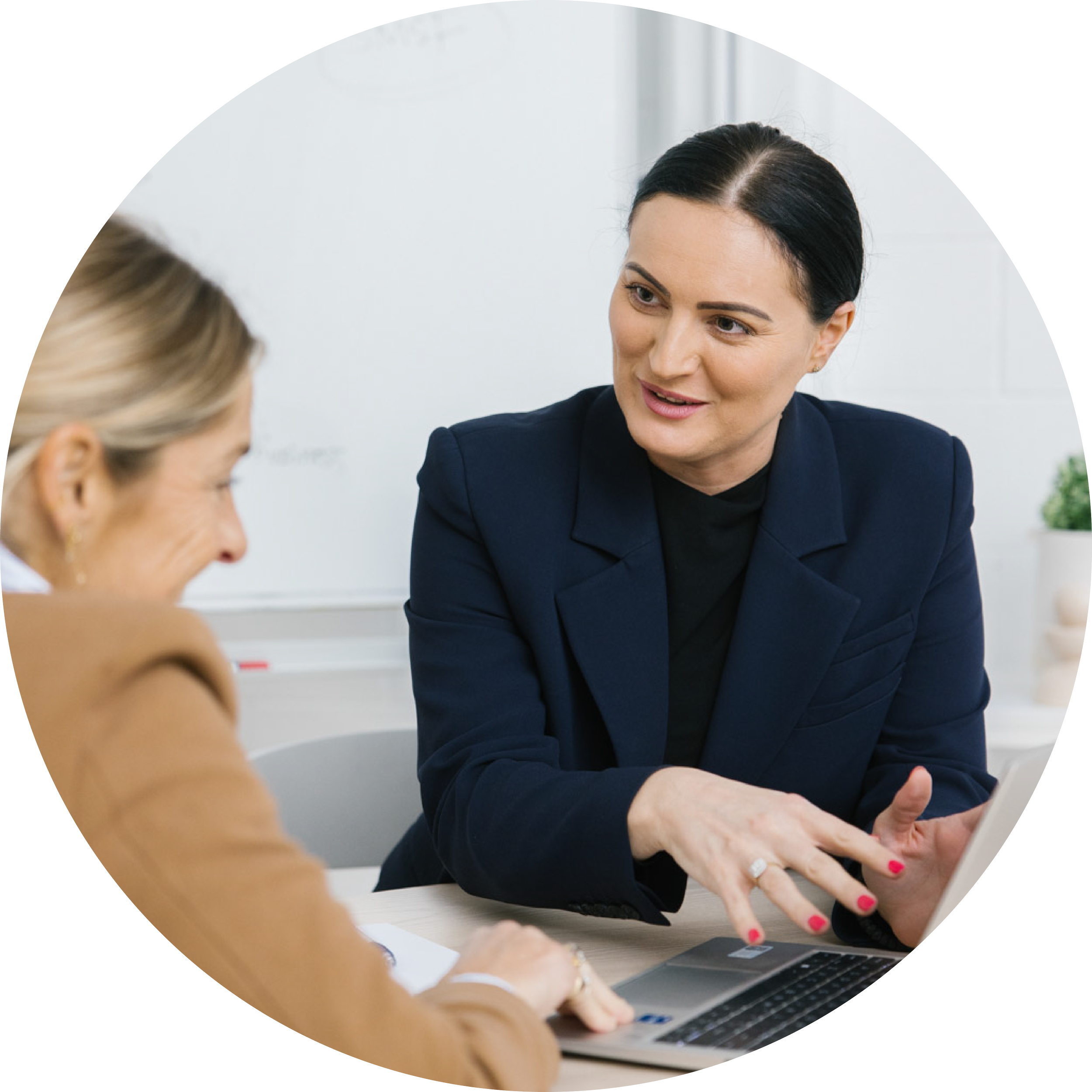 Two women having a professional discussion at a table, one is explaining something on a laptop to the other.