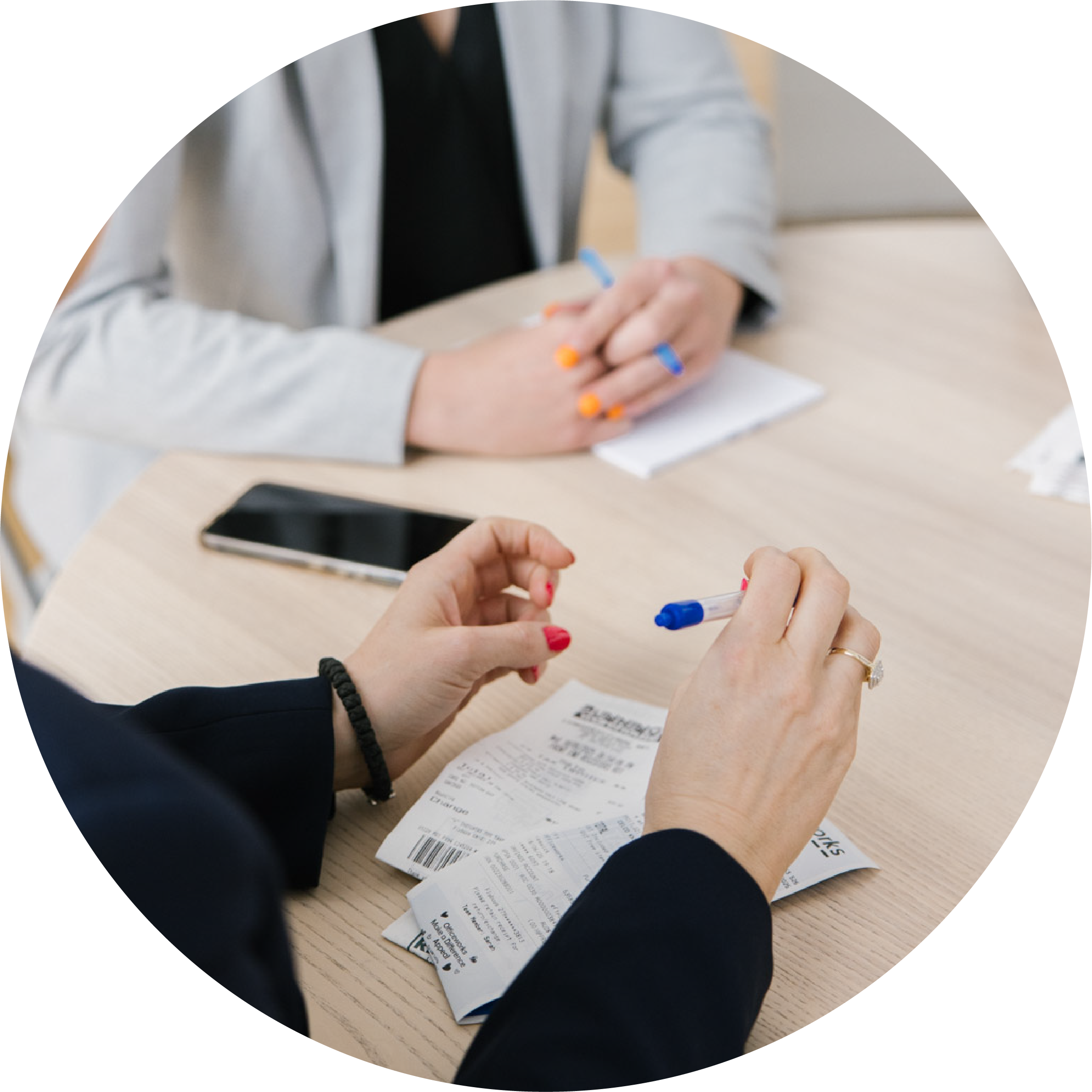 Two people sitting at a table with receipts, a smartphone, and pens, engaged in a discussion about expenses or purchases.