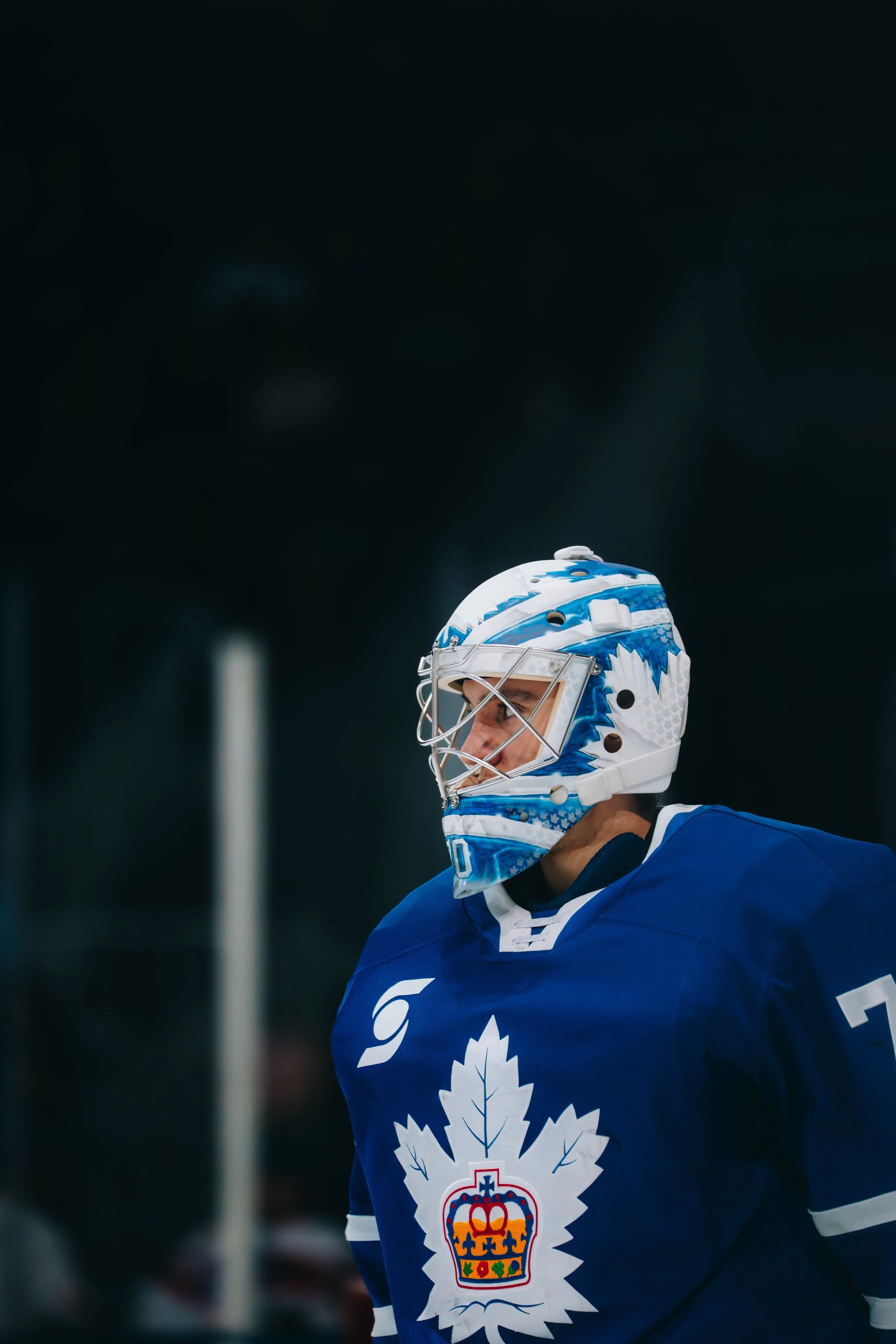A hockey player in a blue jersey and a white, blue, and red helmet with a maple leaf and crest logo.