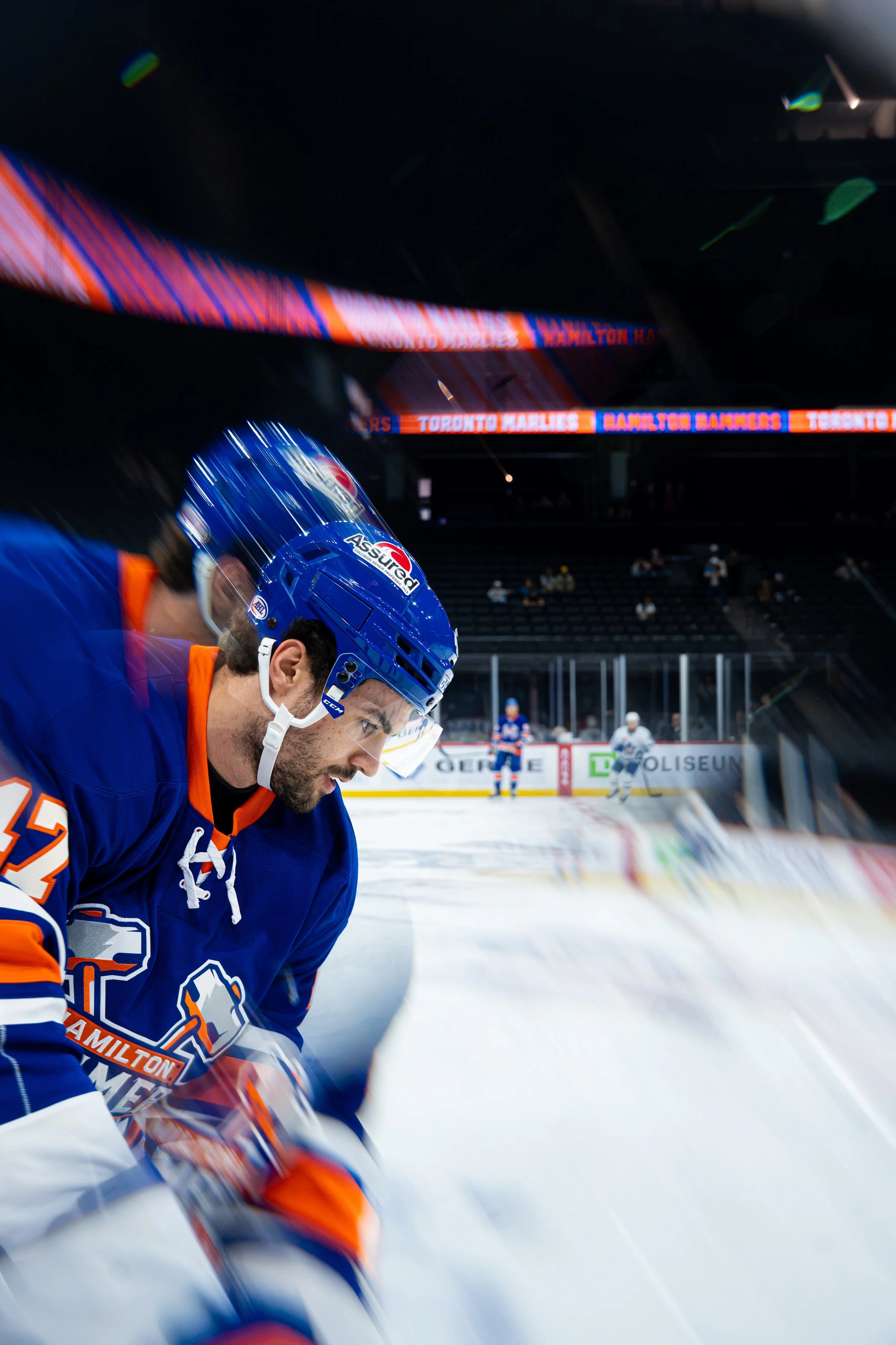 Hockey player wearing blue and orange jersey with helmet, sitting on ice rink during a game at the arena.
