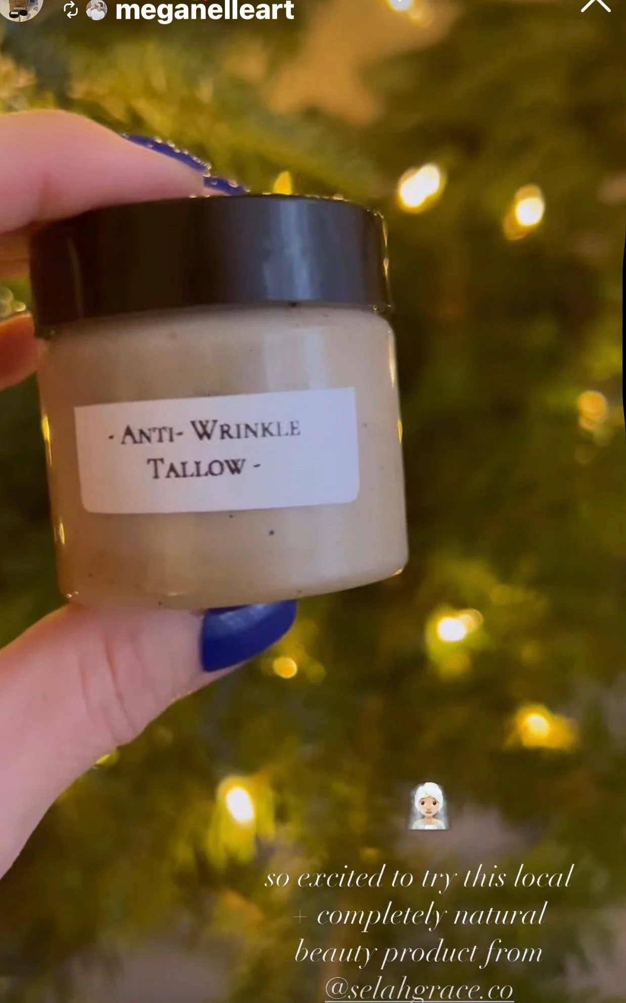 Hand holding a jar labeled 'Anti-Wrinkle Tallow' in front of a decorated Christmas tree with lights.