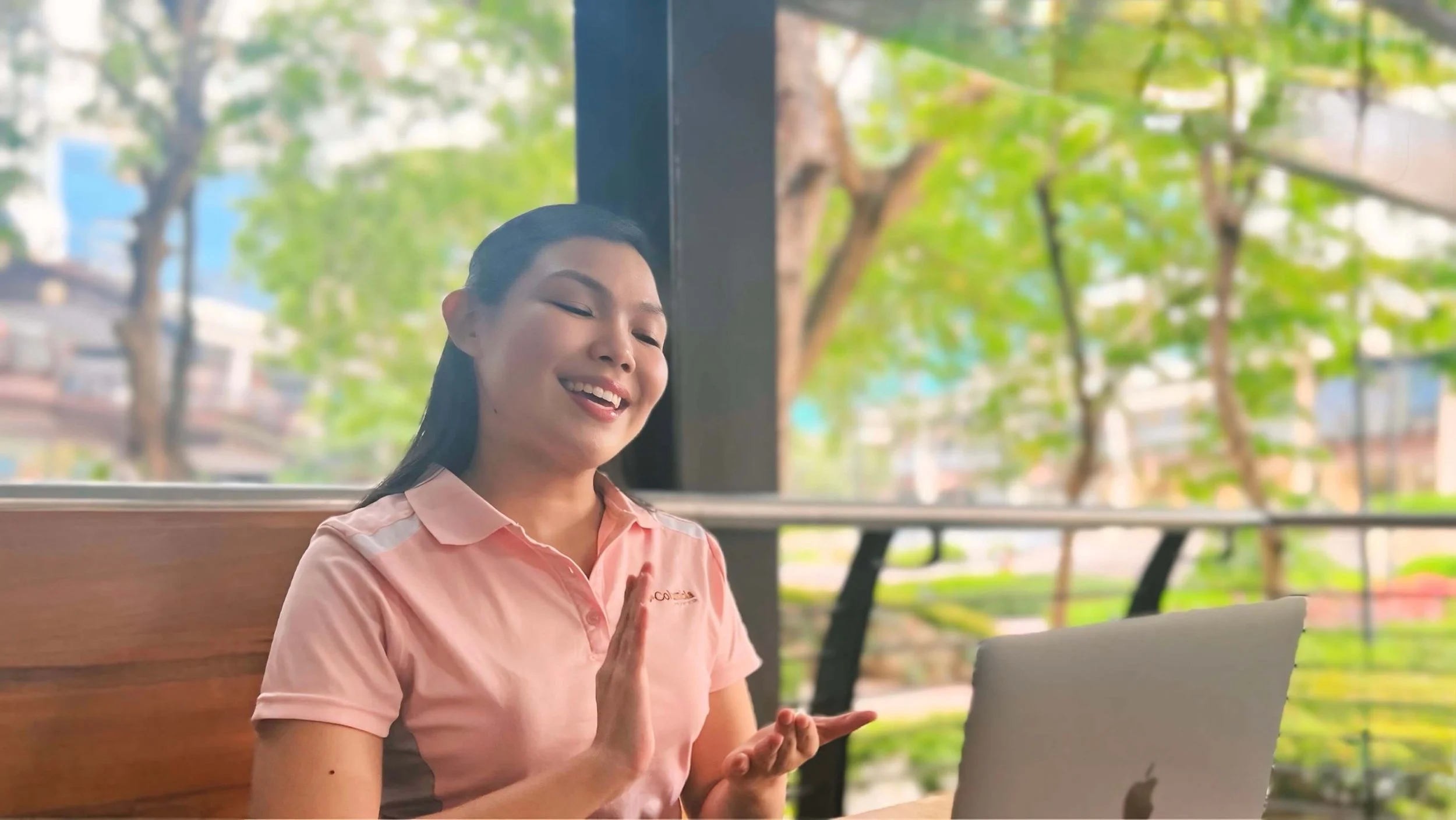 Person in a pink shirt video conferencing on a laptop outdoors.