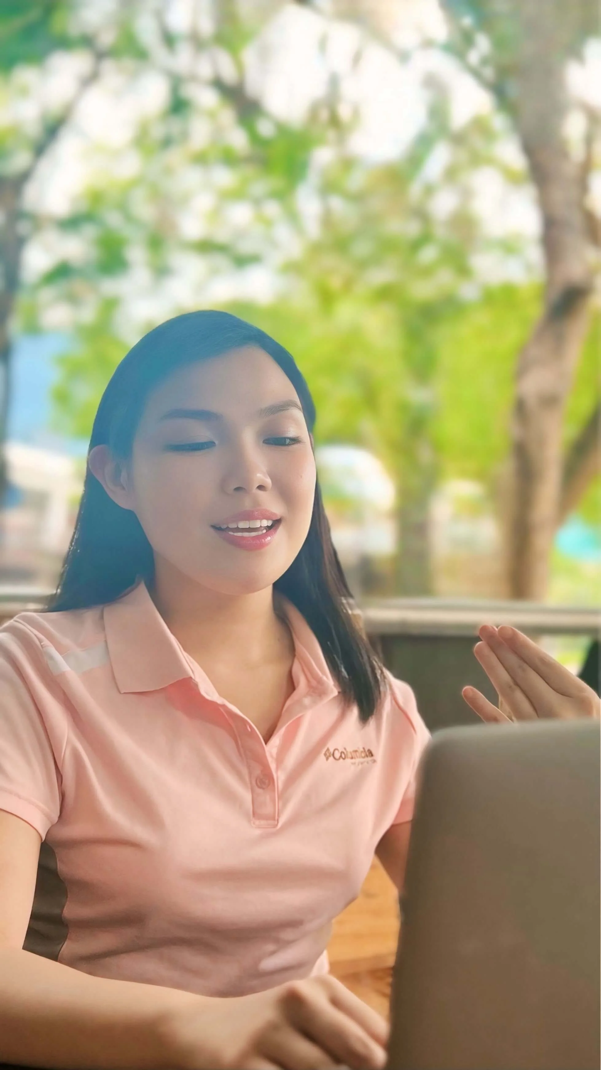 Dietitian in a pink polo shirt speaking, with a blurred outdoor background and a laptop in the foreground.