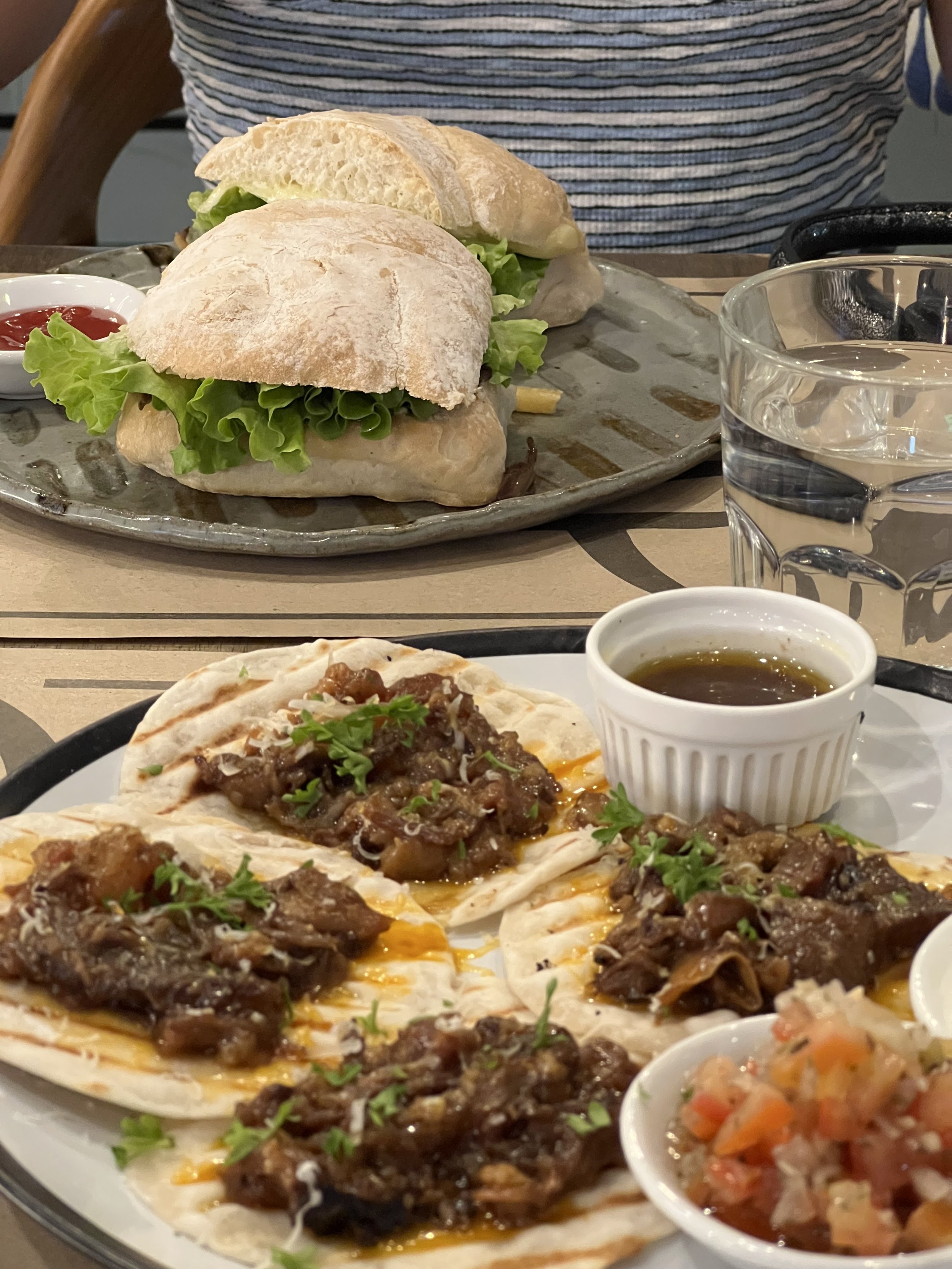 A plate of Mexican Tacos topped with shredded beef, cilantro, and onions served with a side of salsa and a glass of water.