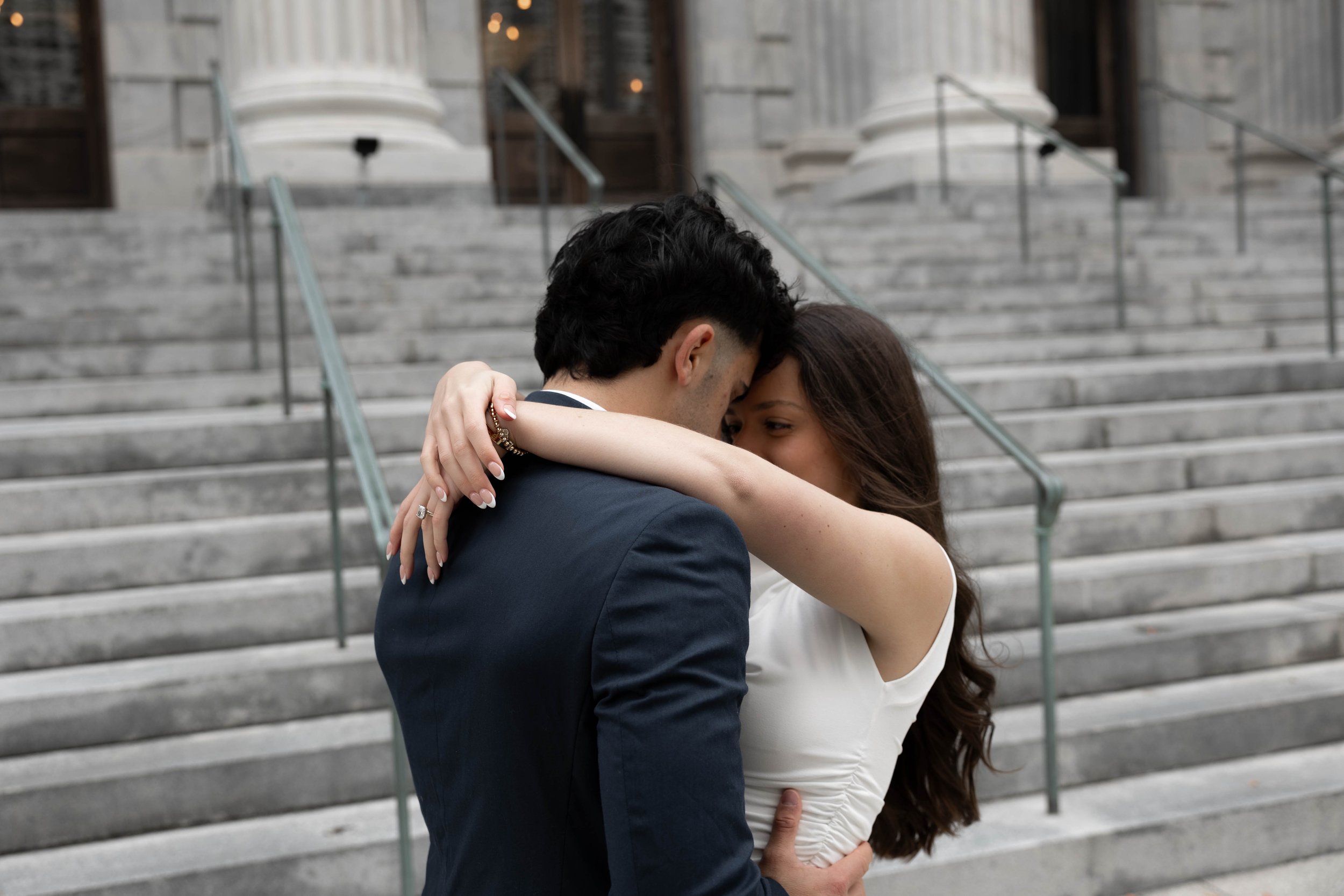 A couple embracing intimately on stone steps in front of a building with columns.