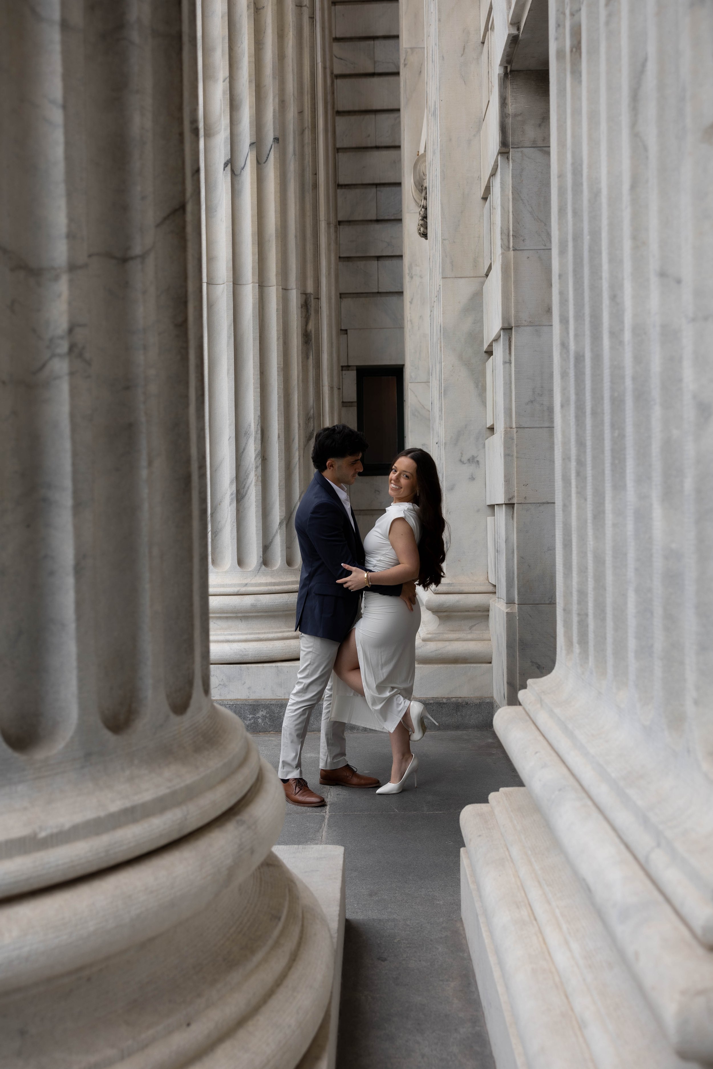Couple embracing between large marble columns.