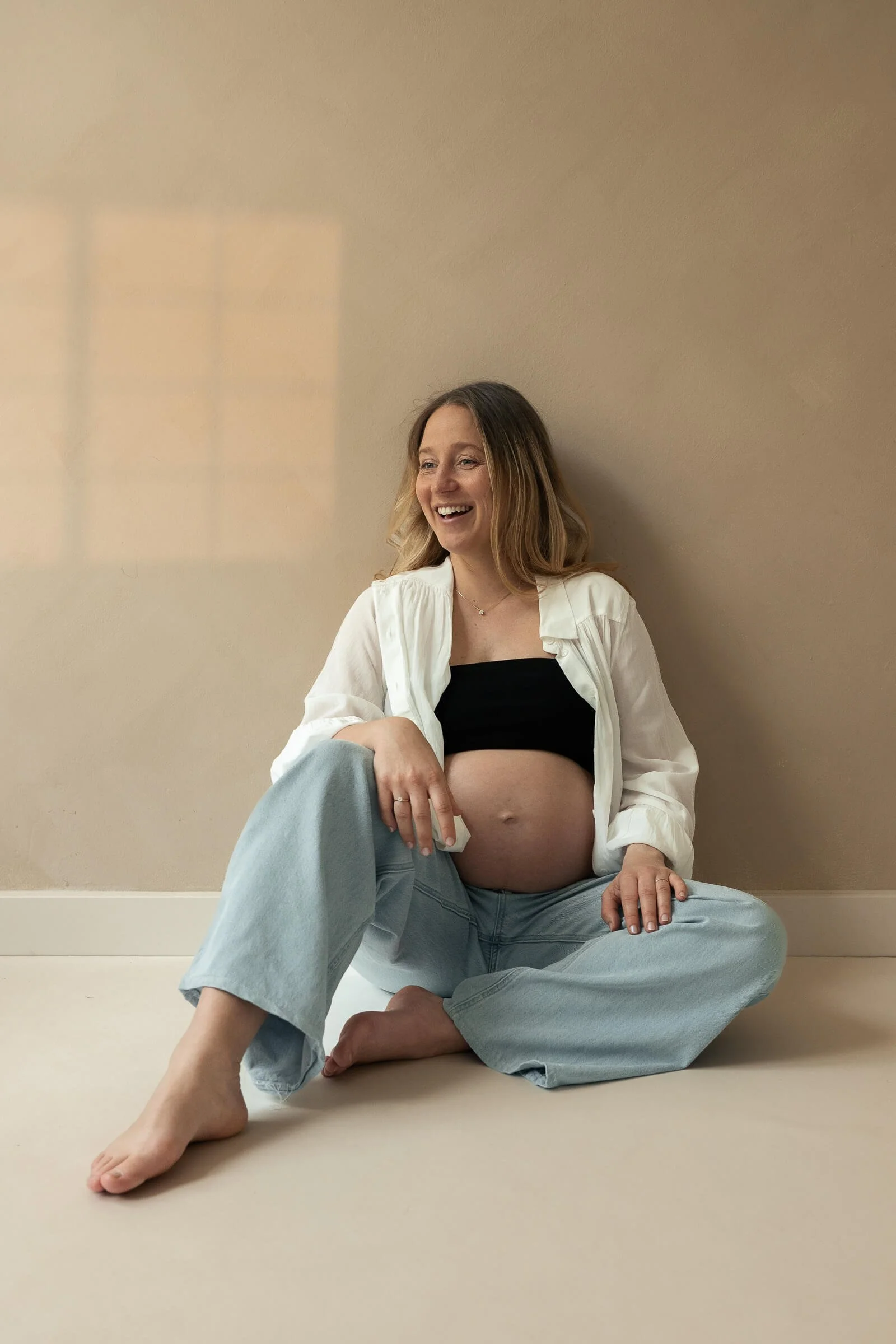 Babybauch Shooting Studio München – lässige schwangere Frau in Jeans und weißem Hemd, Ela Behrens Fotografin