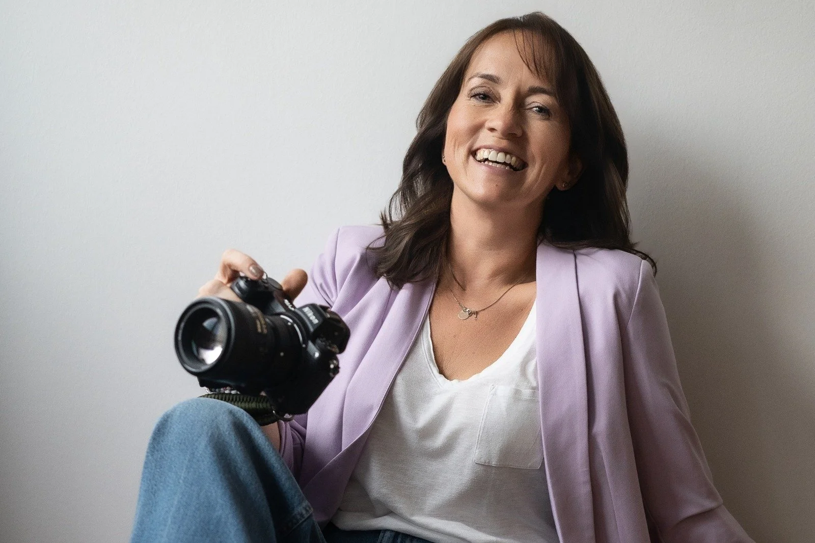 Fotografin sitz mit Kamera entspant am Boden und lacht in die Kamera