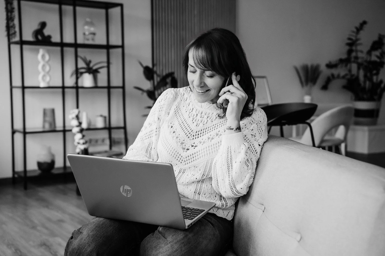 Fotografin sitz mit Kamera entspant auf der Couch und arbeitet am Laptop und telefoniert