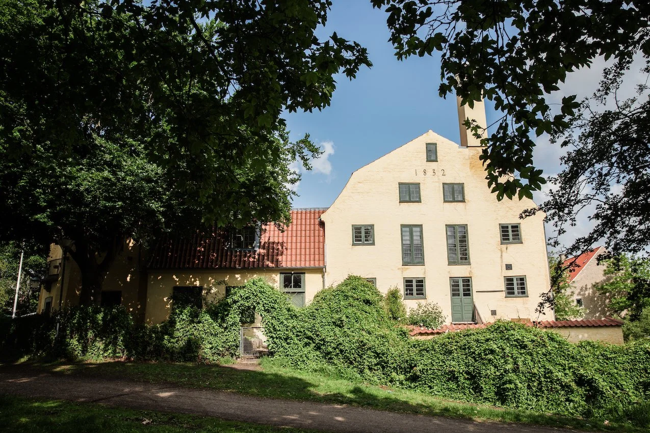 The historic white building at Lille Moelle from 1832, located on Christianshavns Vold with green trees and blue sky.