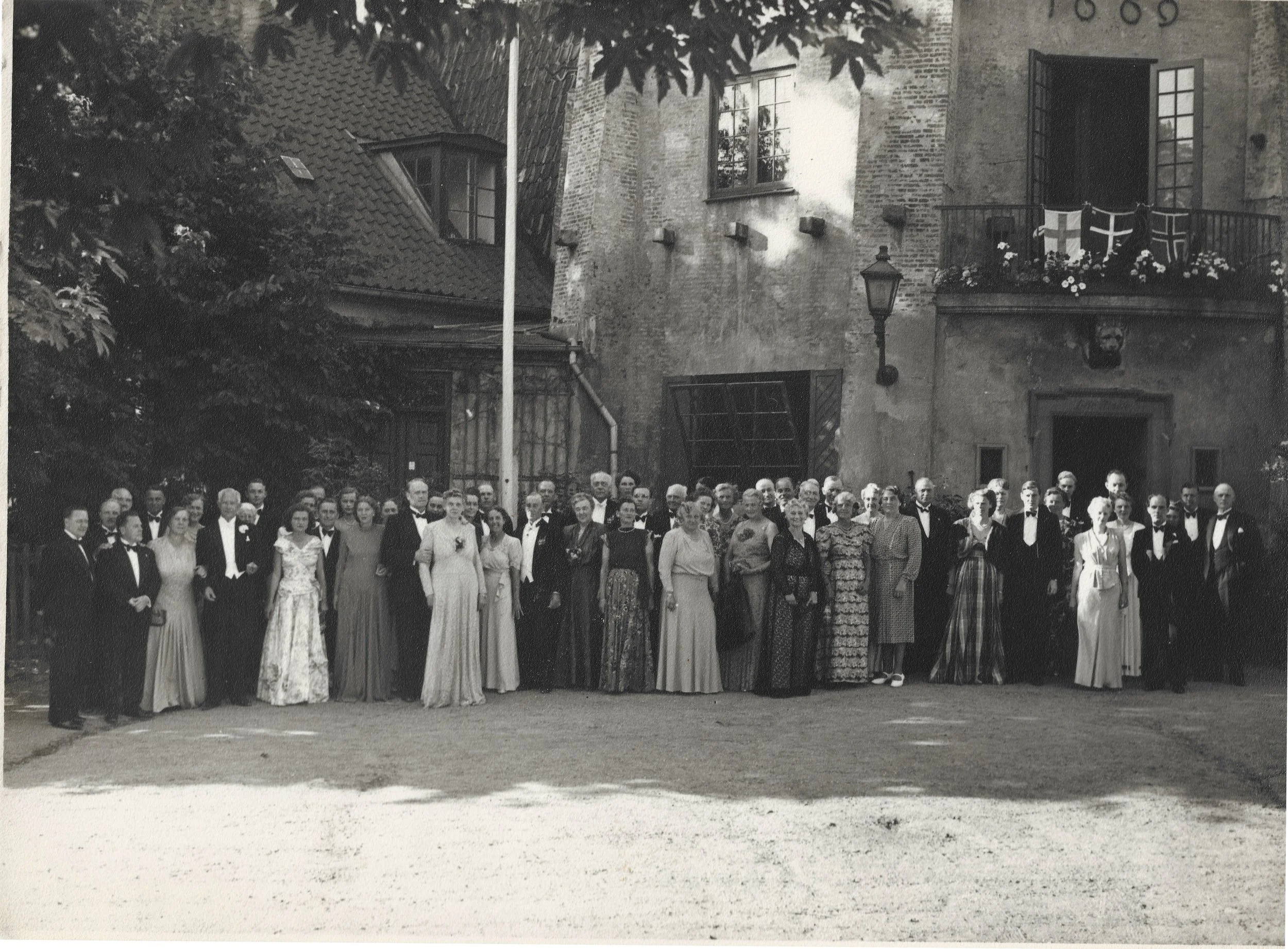 An archival black and white photograph of a formal group gather outside the historic Lille Moelle building, representing traditions and heritage.