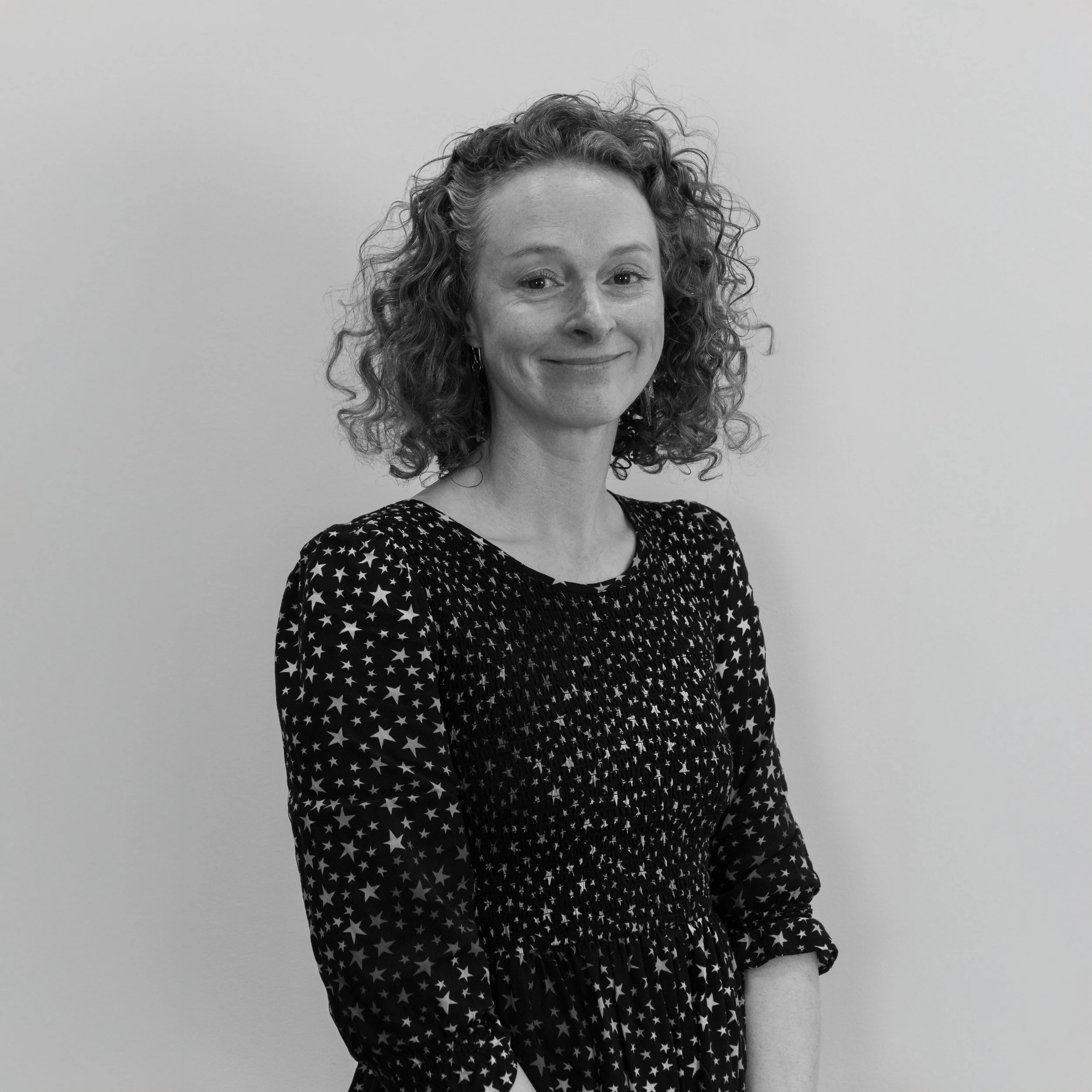 A woman with curly hair smiling and wearing a star-patterned dress.